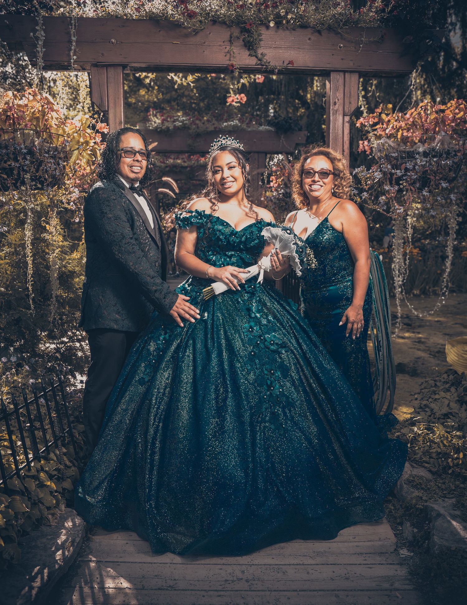 Three people pose together in formal attire with teal gown as centerpiece.