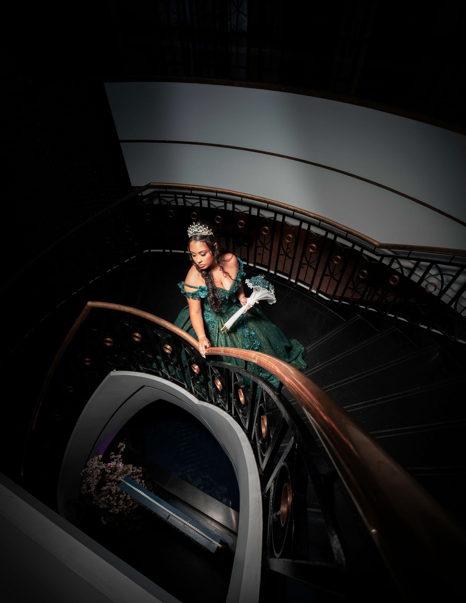 Dramatic photo of a person in a teal gown posing on an elegant spiral staircase.