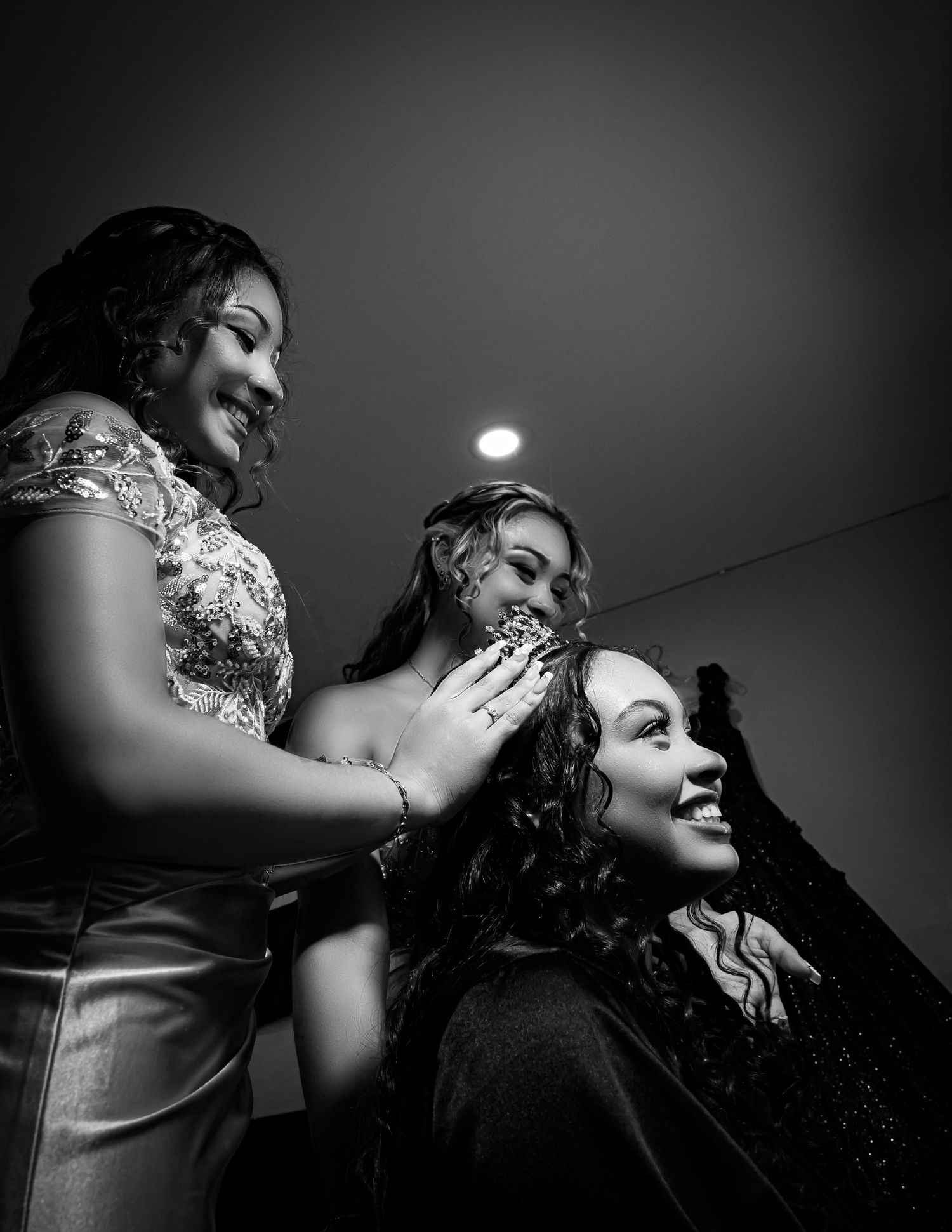 A black and white candid moment shows three people laughing and sharing a joyful moment together in dramatic lighting.