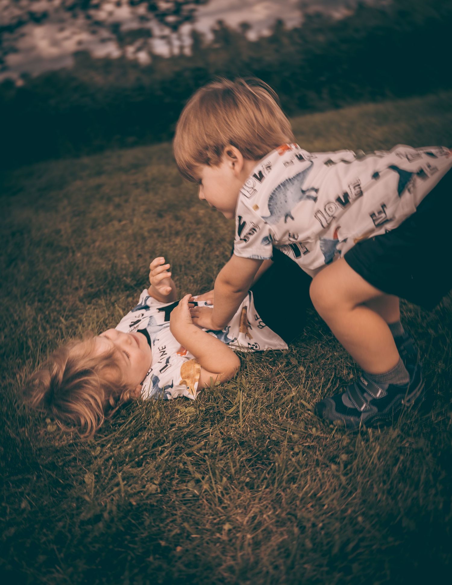 Two children playing and laughing together on green grass in vintage toned lighting.