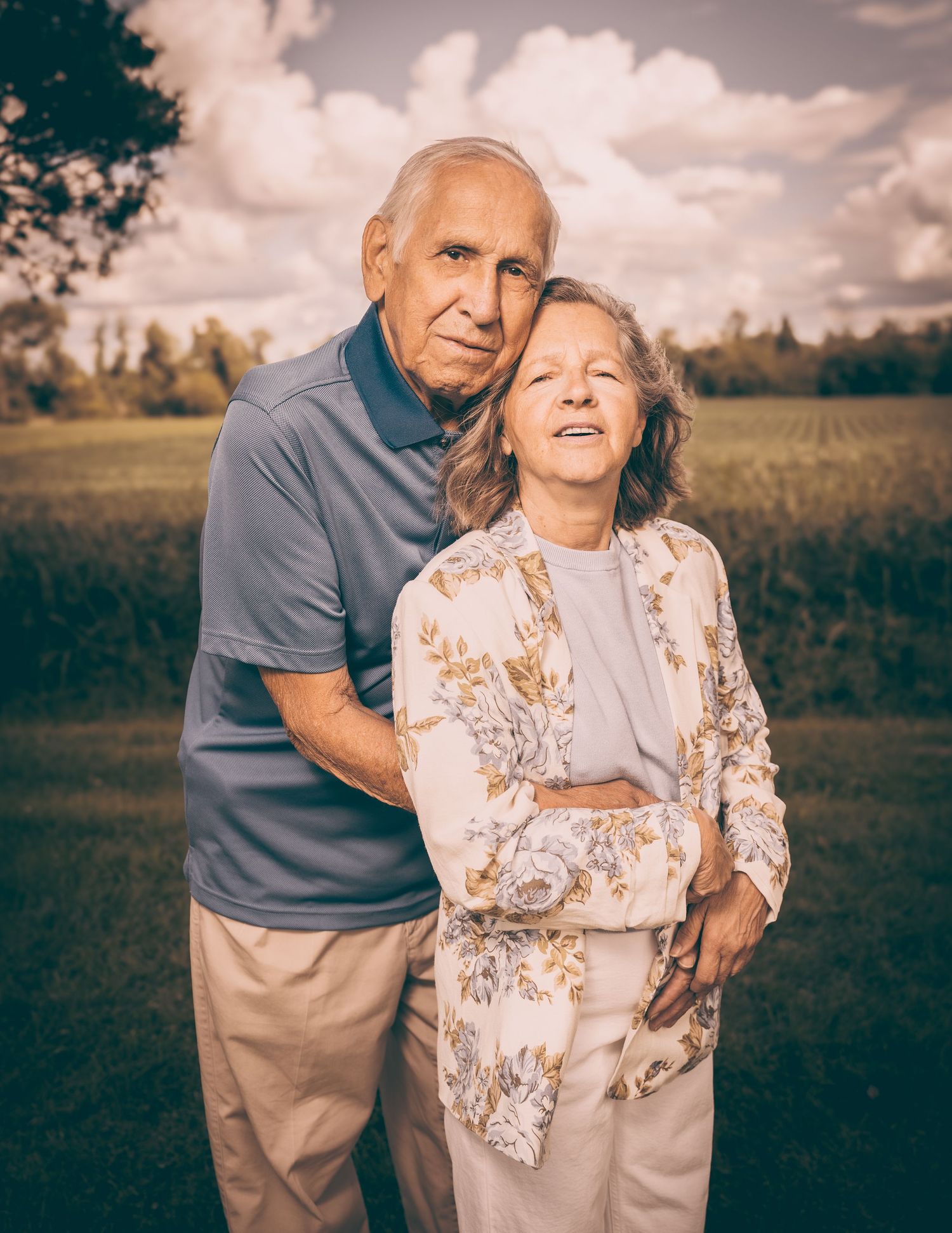 Elderly couple embracing in warm sunlight against a pastoral landscape.