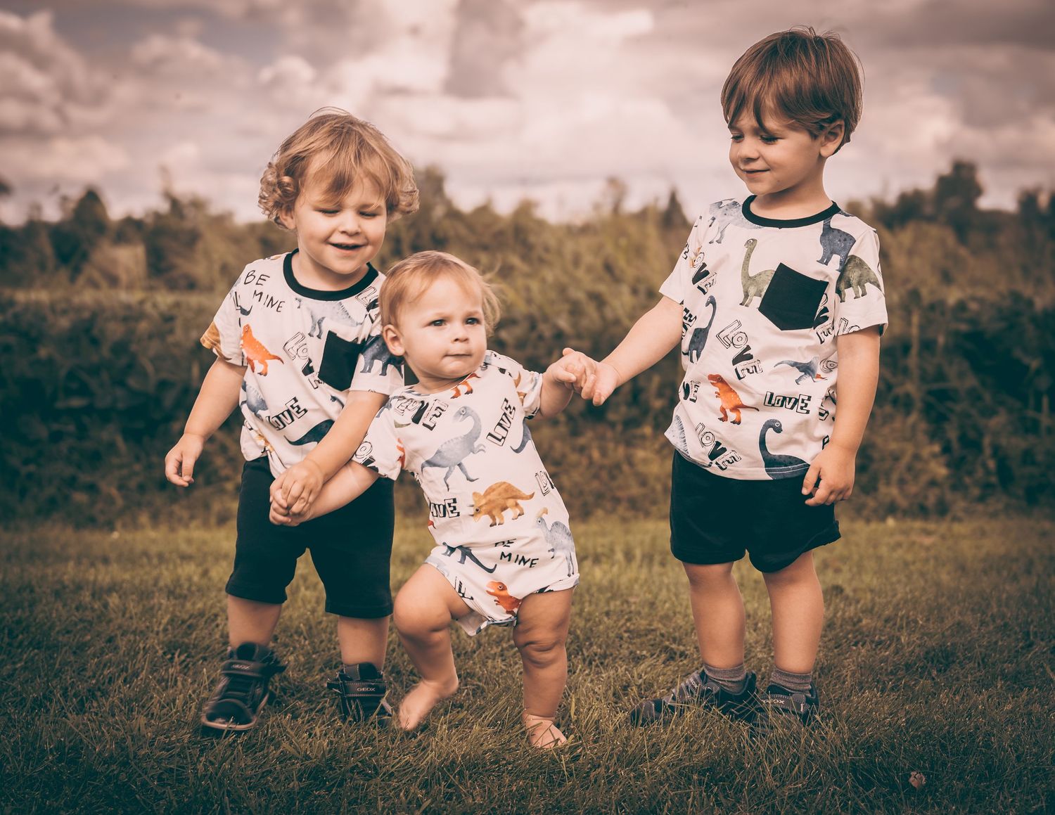Three young children in matching dinosaur print shirts playing together outdoors.
