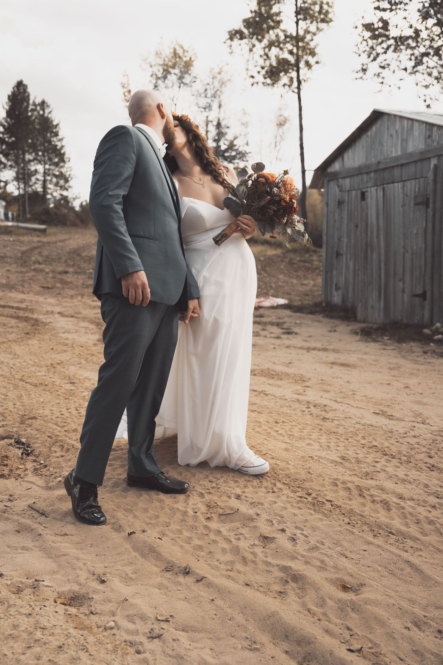 A couple shares an intimate moment together on a dirt path beside a rustic barn on their autumn wedding day.