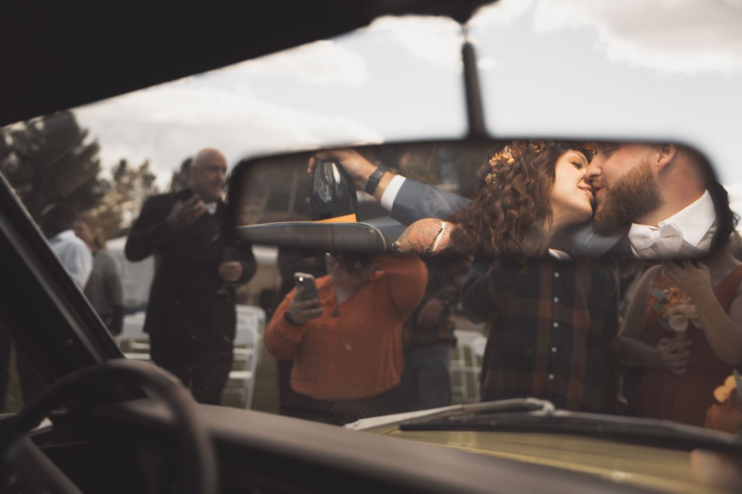 Through a car window reflection, people interact while dressed in warm clothing on an overcast day.