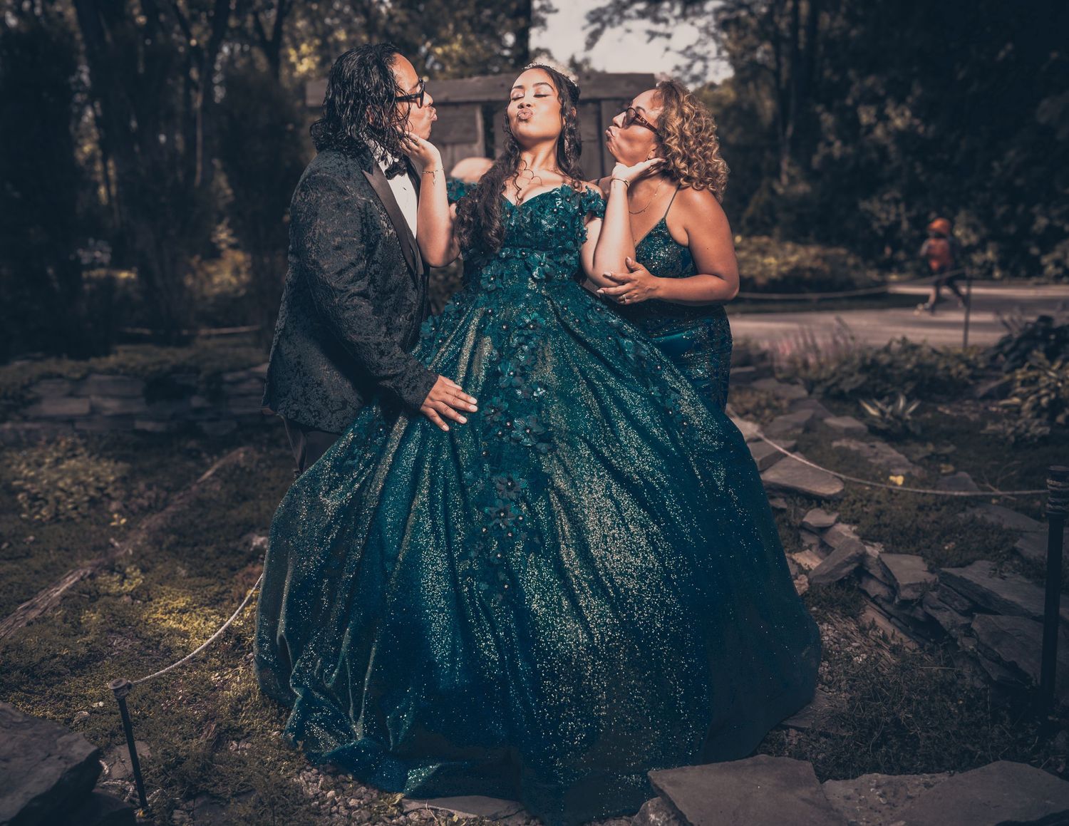 A group poses playfully outdoors with someone wearing a stunning teal sequined ballgown.