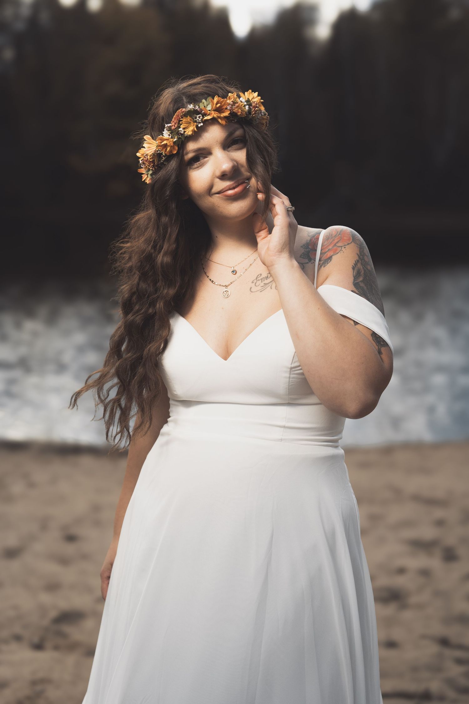 A bride in a white dress and orange floral crown poses outdoors with a dreamy expression.