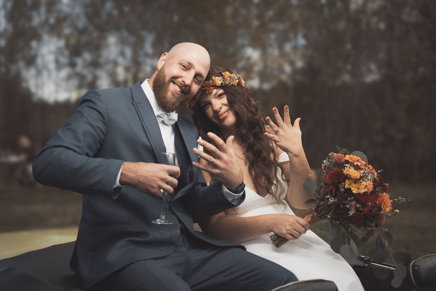 A happy couple laughs together on their wedding day while holding a bouquet of autumn flowers.