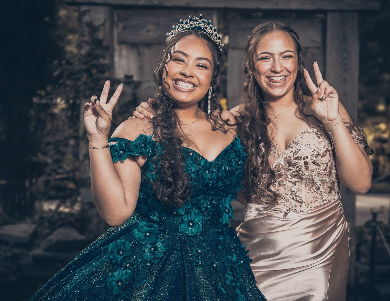 Two friends pose together at a formal event, one in a sparkly teal gown and one in champagne satin.