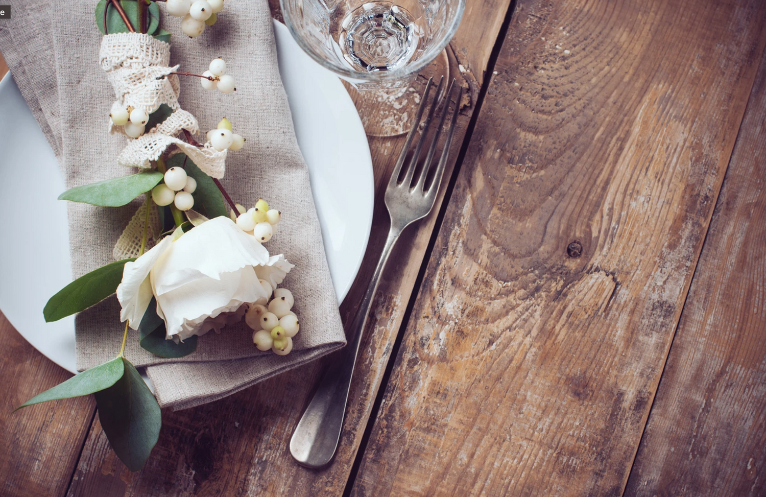 A rustic table setting with white flowers, silverware and distressed wooden surface creates an elegant vintage atmosphere.