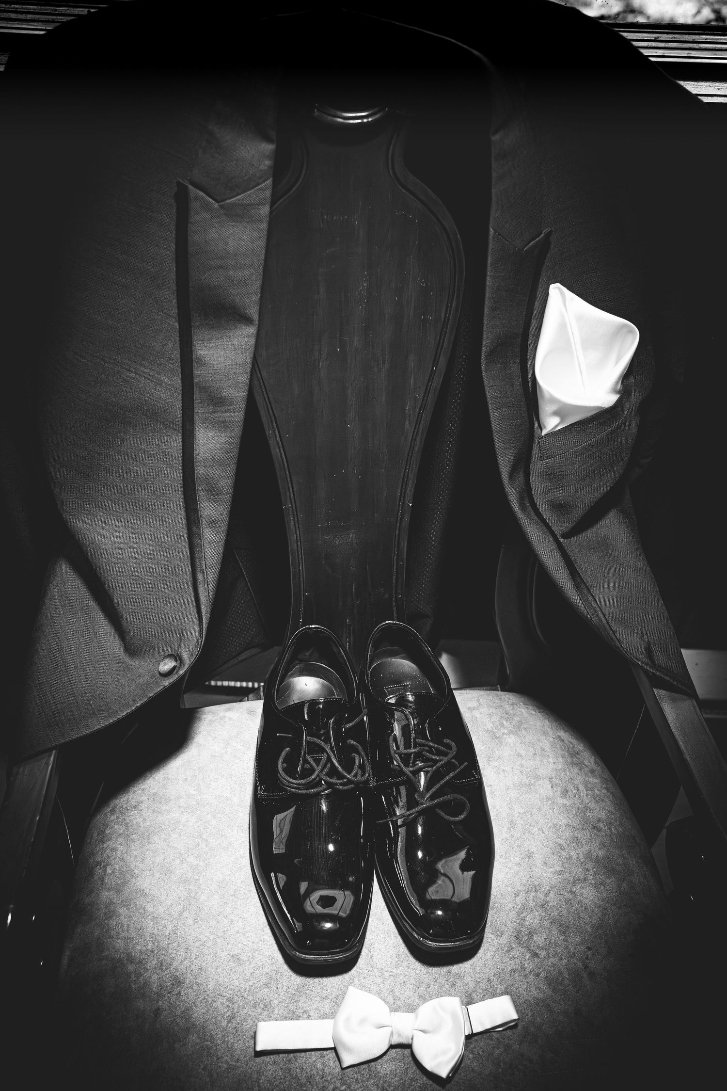 Black and white photo of formal men's dress shoes and bow tie arranged on dark surface.