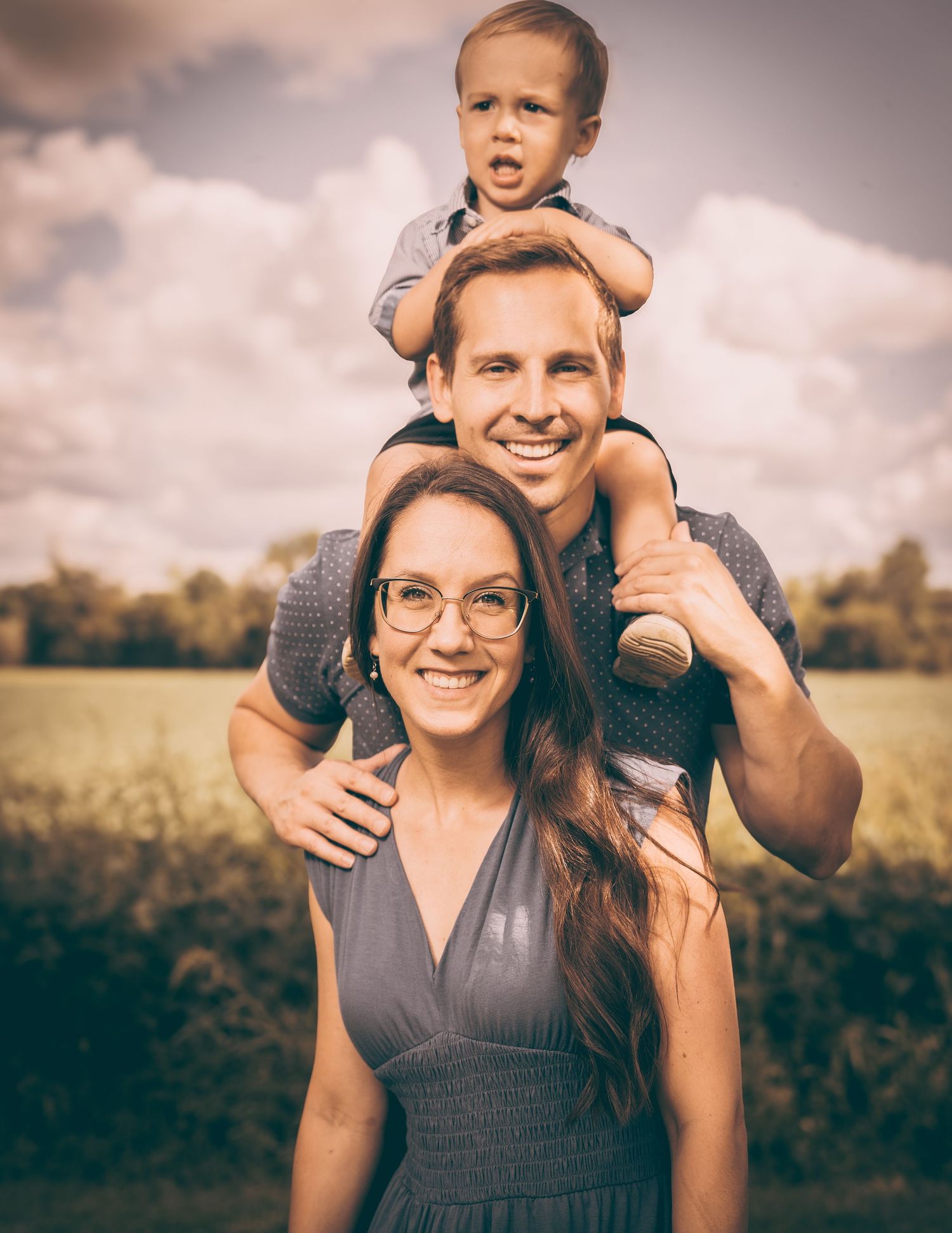 Happy family portrait with playful child sitting on shoulders outdoors.