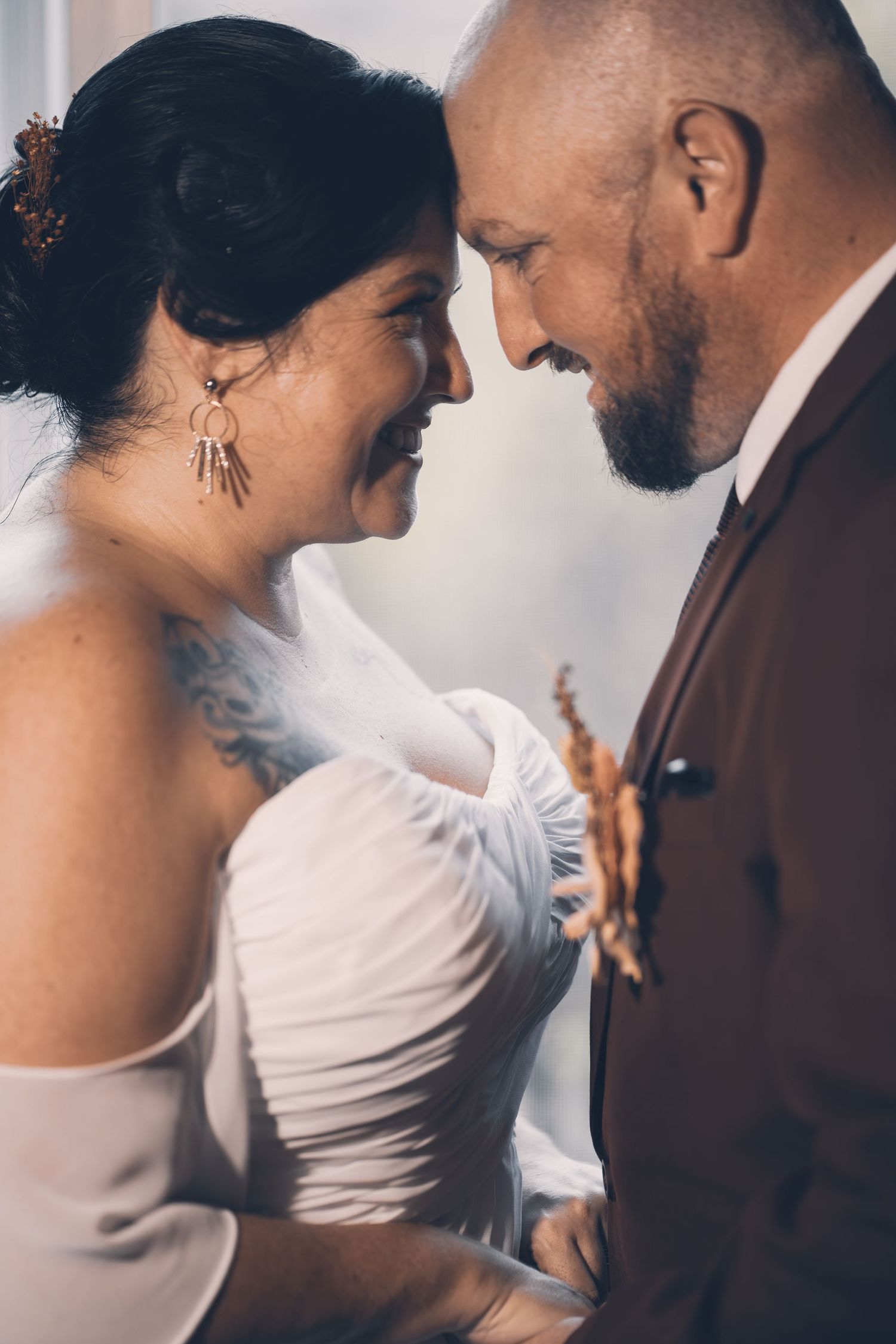 A tender wedding moment between a bride in white and groom in brown suit as they share an intimate close-up moment.