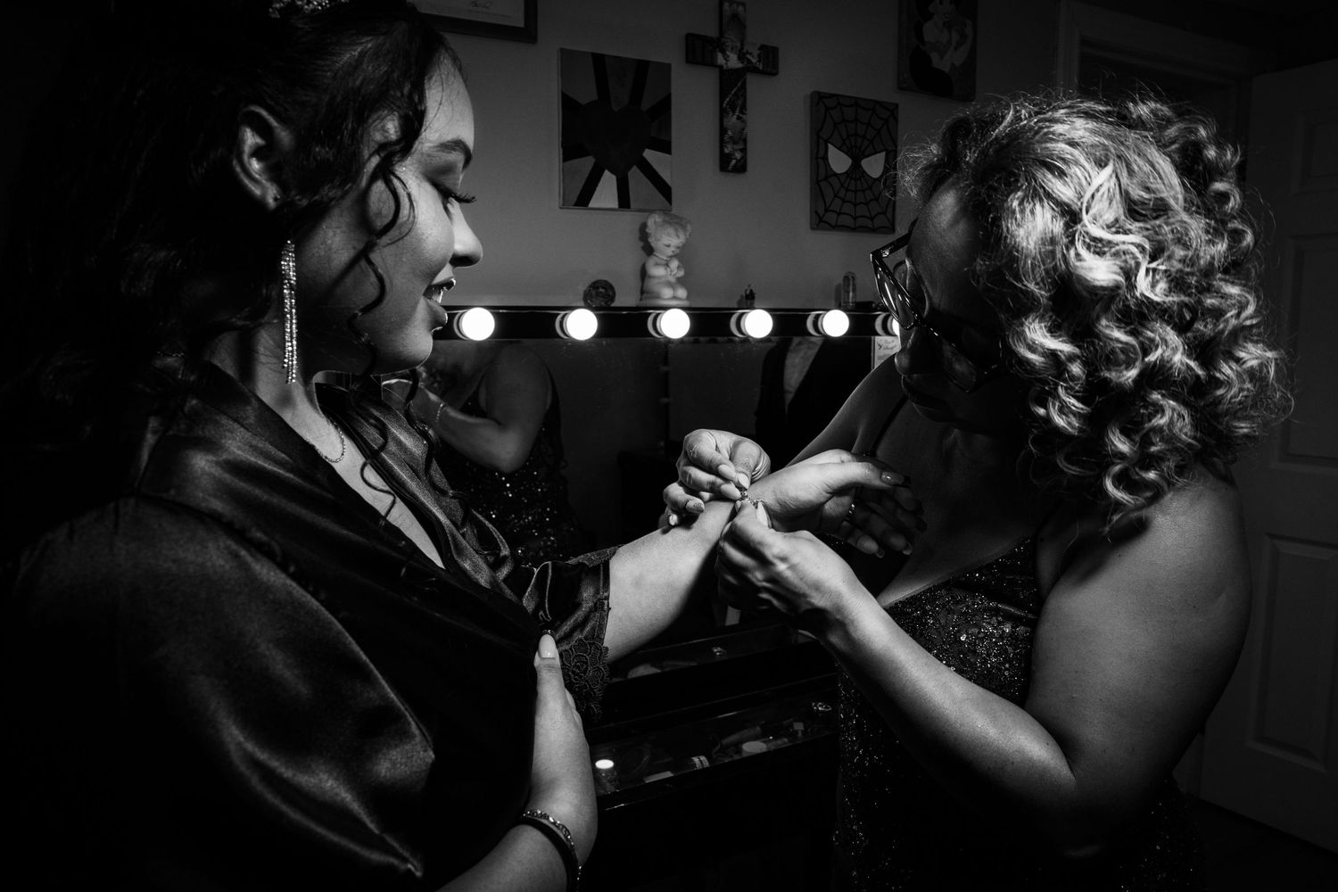 Black and white photo of two performers adjusting costumes backstage with vanity lights glowing in the background.