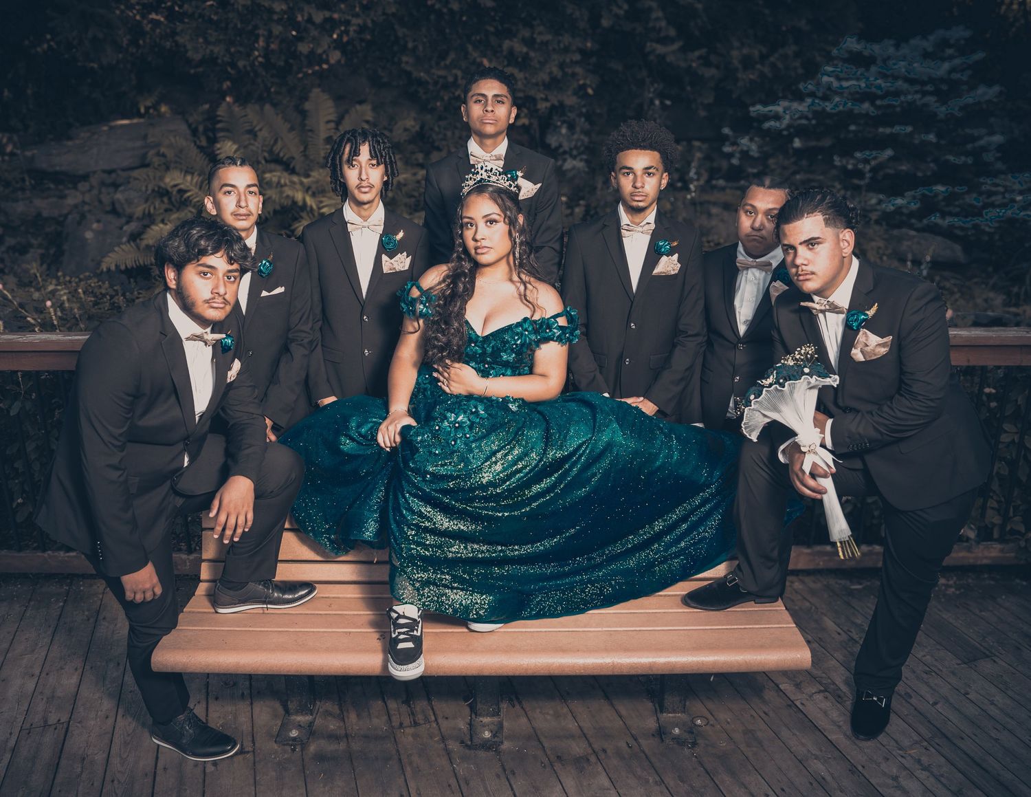 Group portrait of wedding party members in formal attire on wooden deck.
