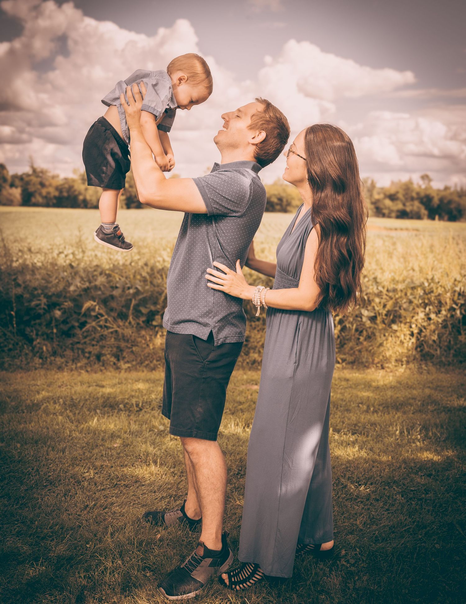Young couple in casual clothes playing with their baby in a sun-lit meadow.