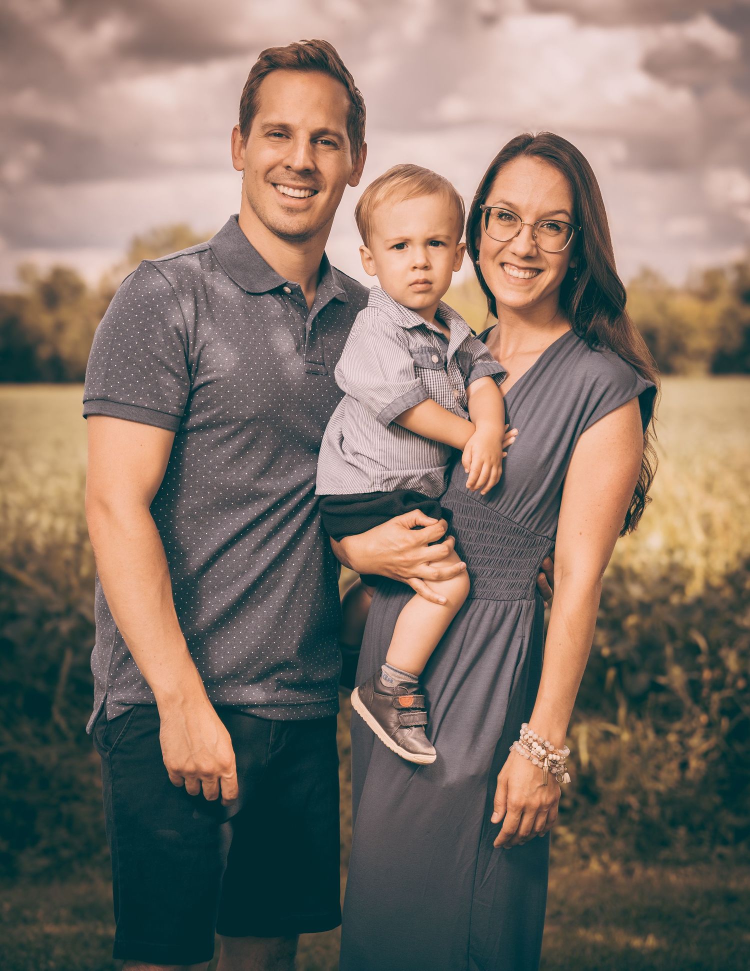 Young family poses together in a golden field during sunset.