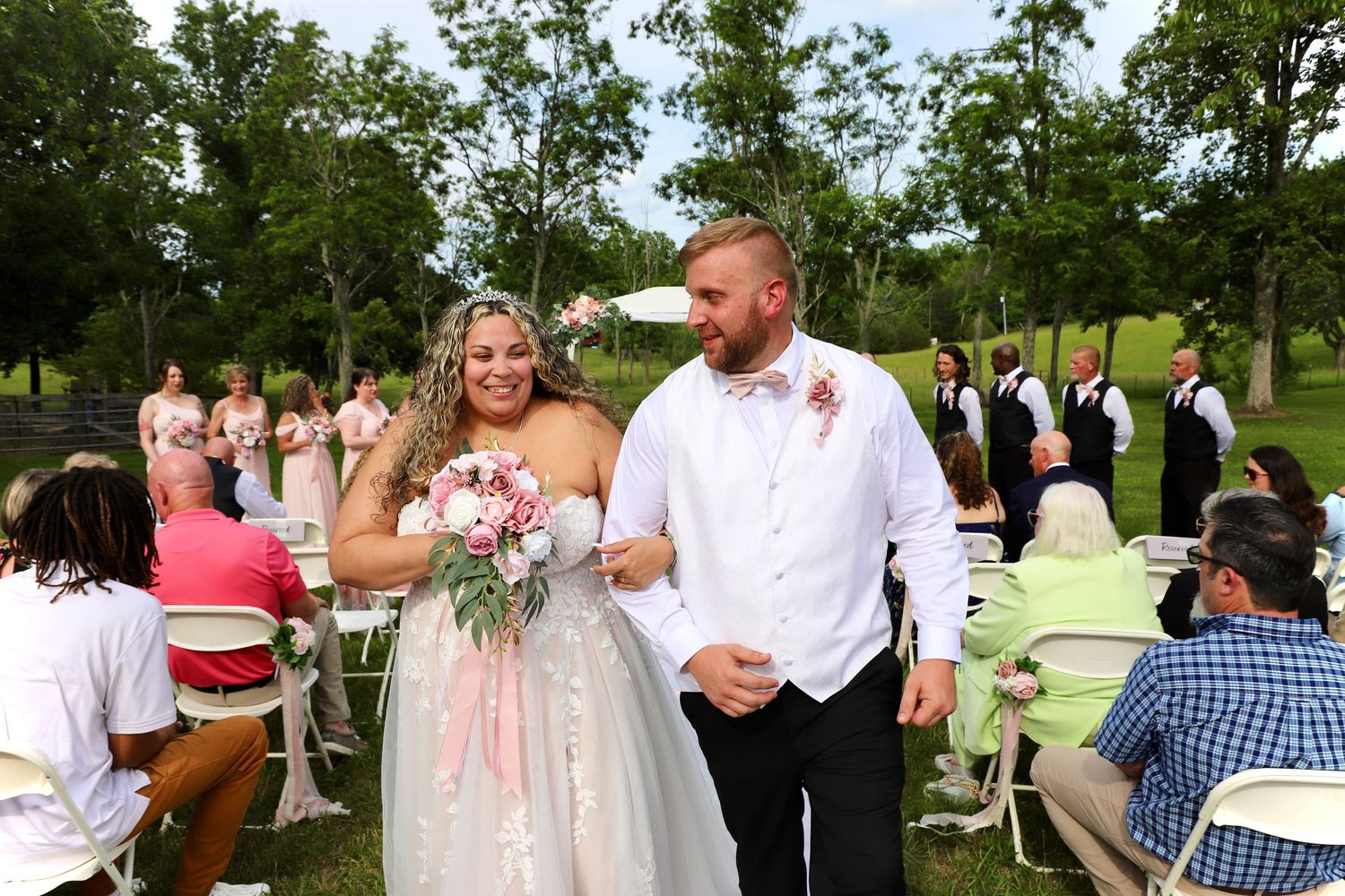 Newlywed couple walking joyfully down the aisle after outdoor wedding ceremony with guests seated.