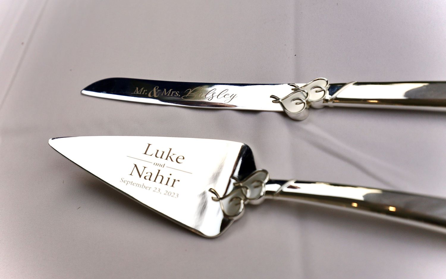 Engraved silver wedding cake knife and server set personalized with Luke and Nahir on elegant display.