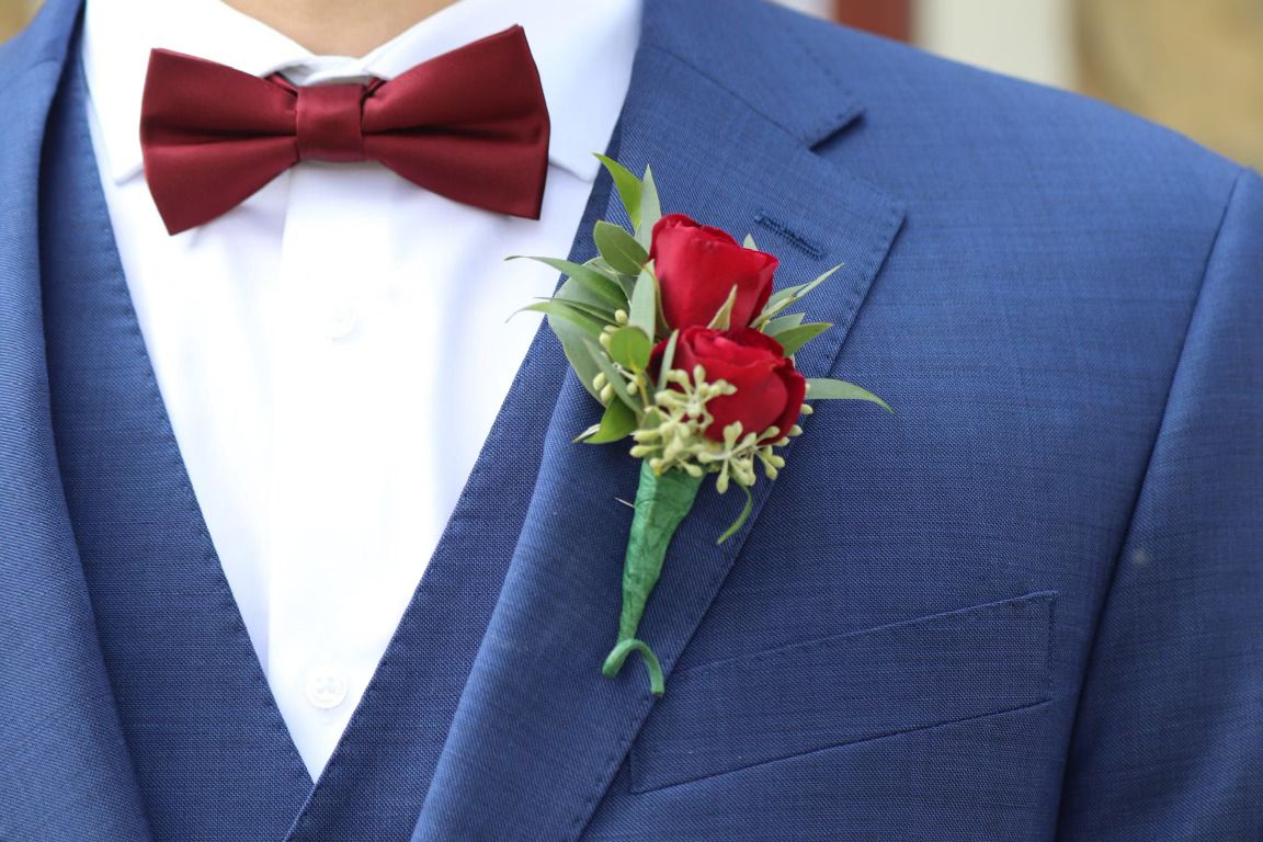 Groom in blue suit with red rose boutonniere and burgundy bow tie at wedding ceremony.