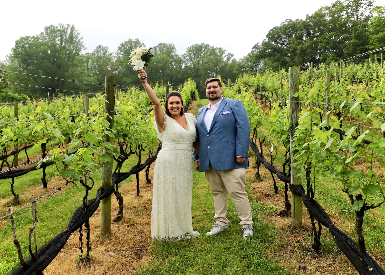 Joyful newlywed couple celebrating their wedding day among lush green vineyard rows outdoors.