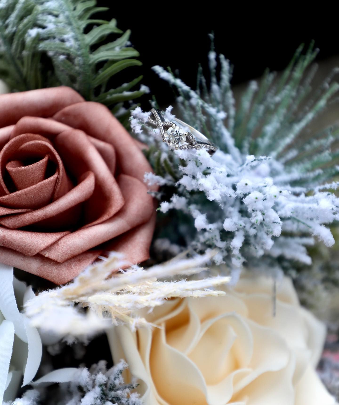 Diamond engagement ring nestled among frosted winter roses and pine in bridal bouquet.