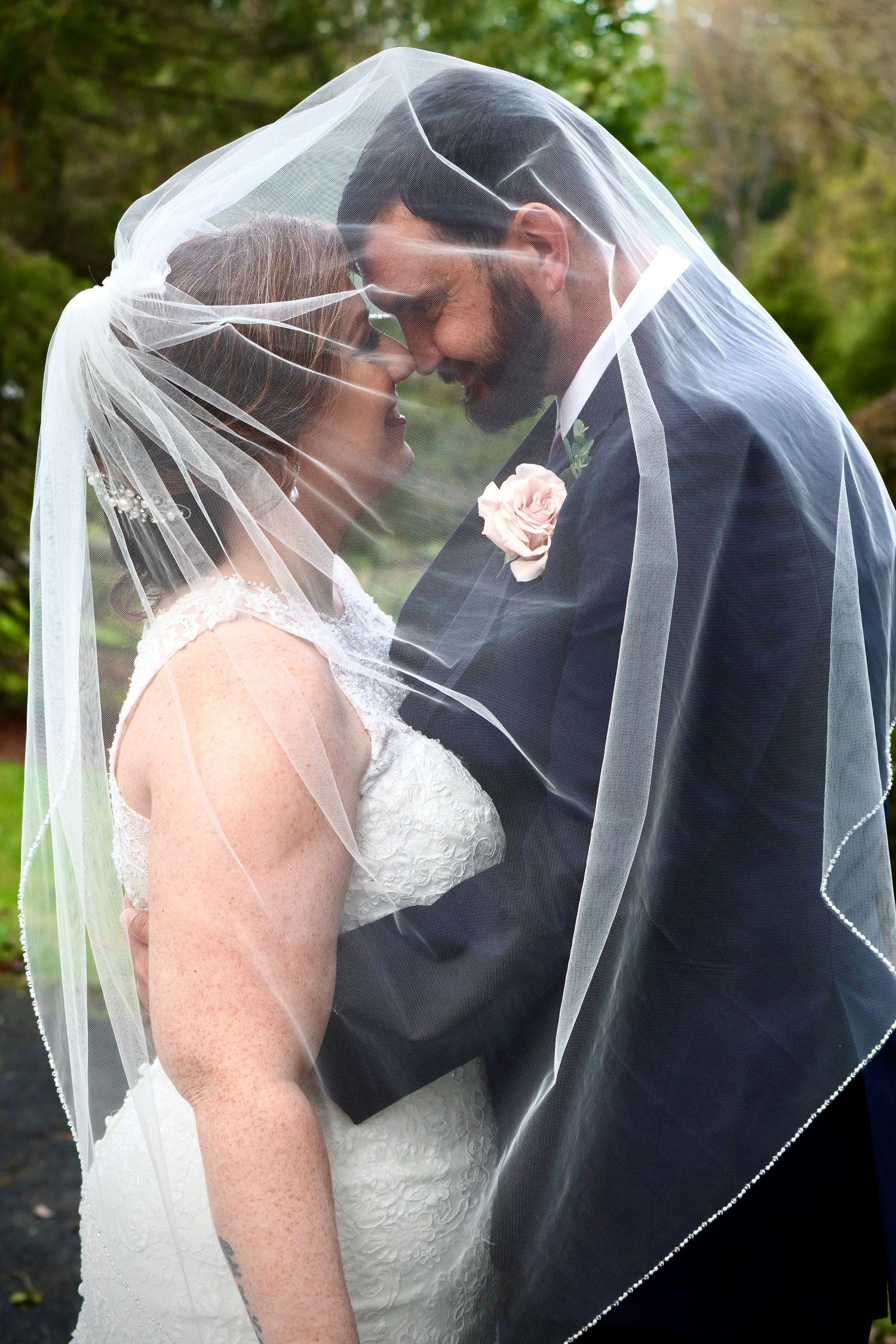 Romantic bride and groom sharing an intimate moment together under a flowing white wedding veil outdoors.