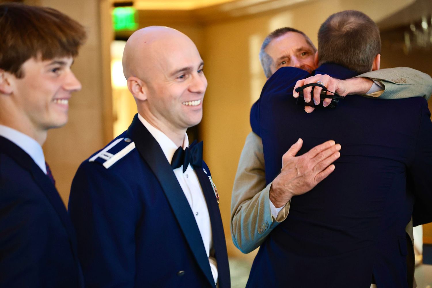 Smiling military groom in dress uniform greeting wedding guests in a bright reception hall.