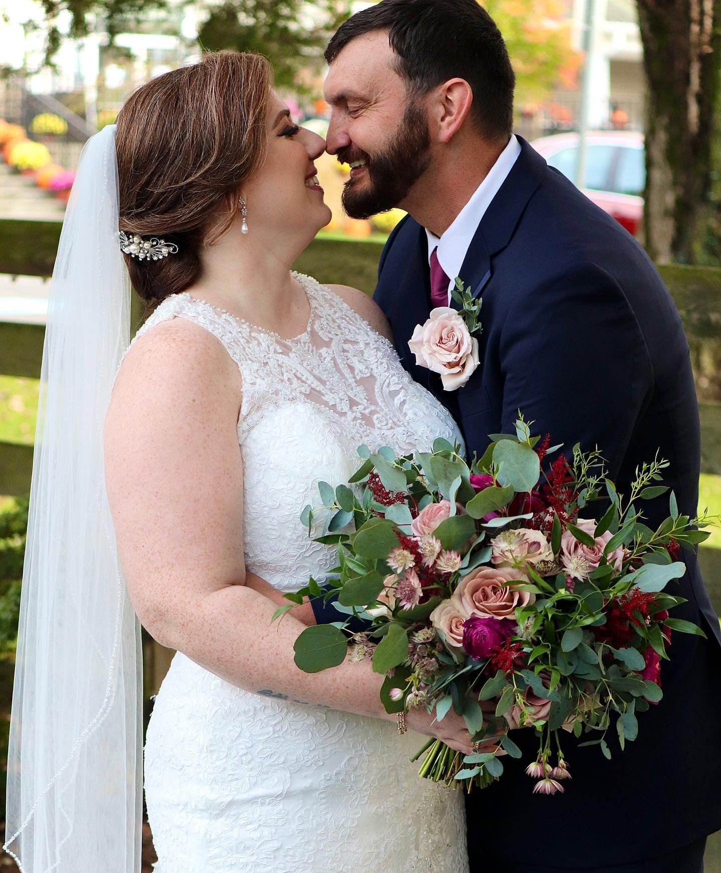 A wedding couple shares an intimate moment with a beautiful burgundy and pink floral bouquet.