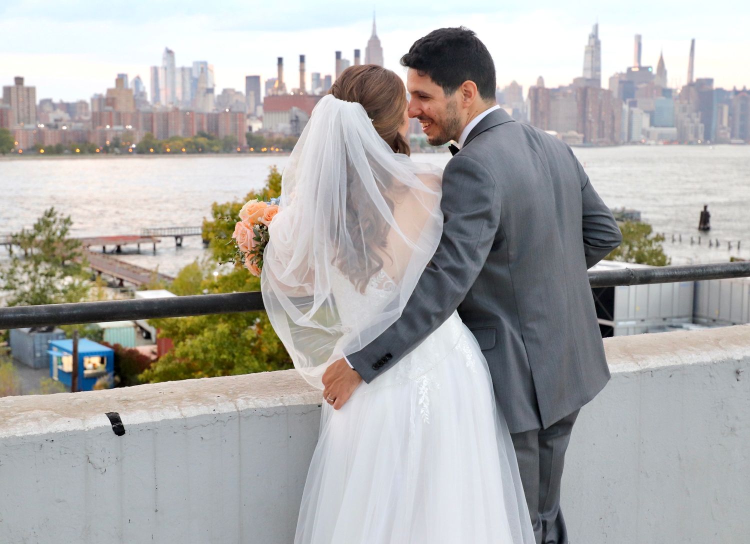 Bride and groom sharing kiss on rooftop venue with stunning New York City skyline backdrop.