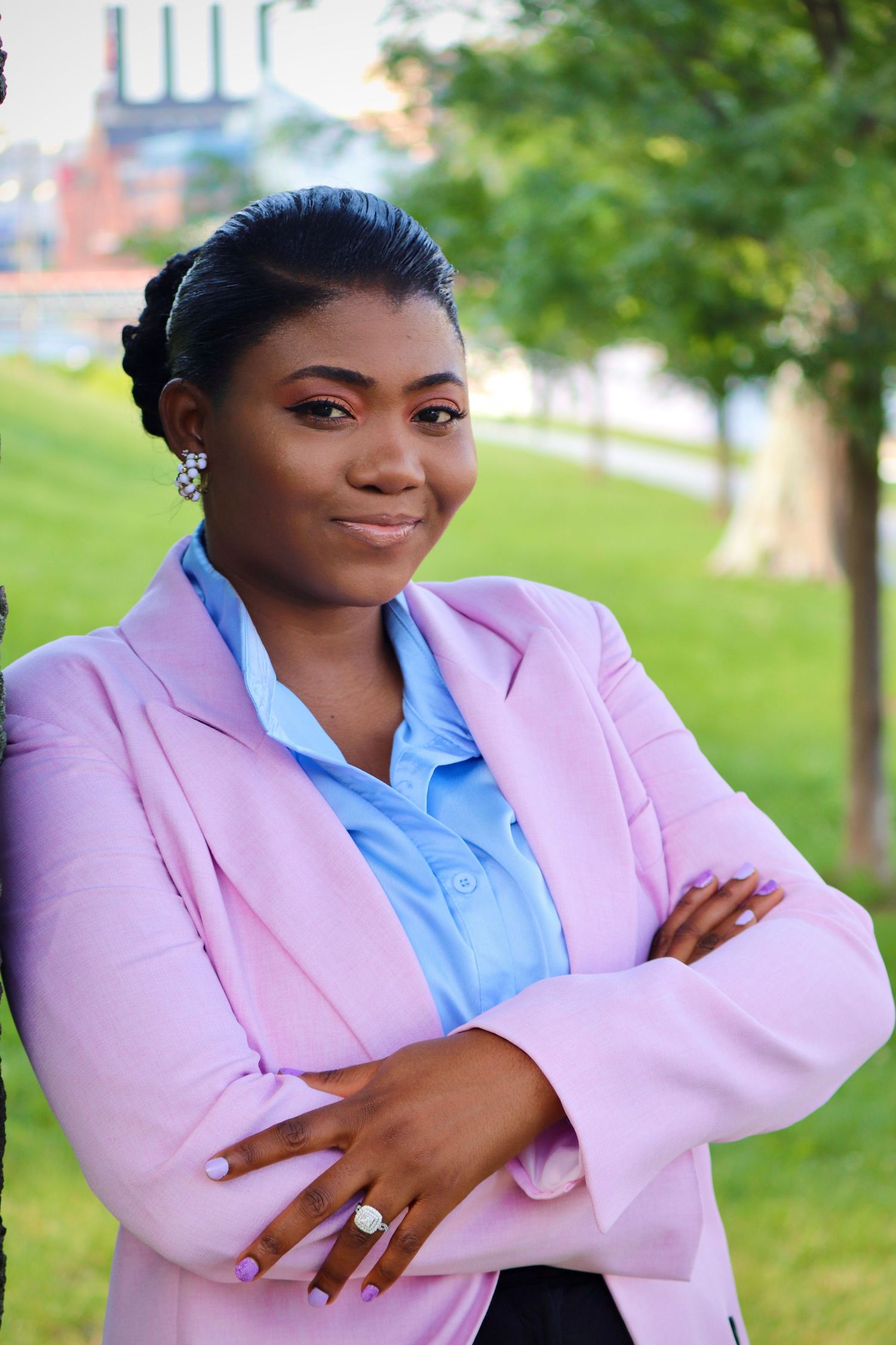 Professional portrait of someone in a pink blazer and blue shirt against a green park background.