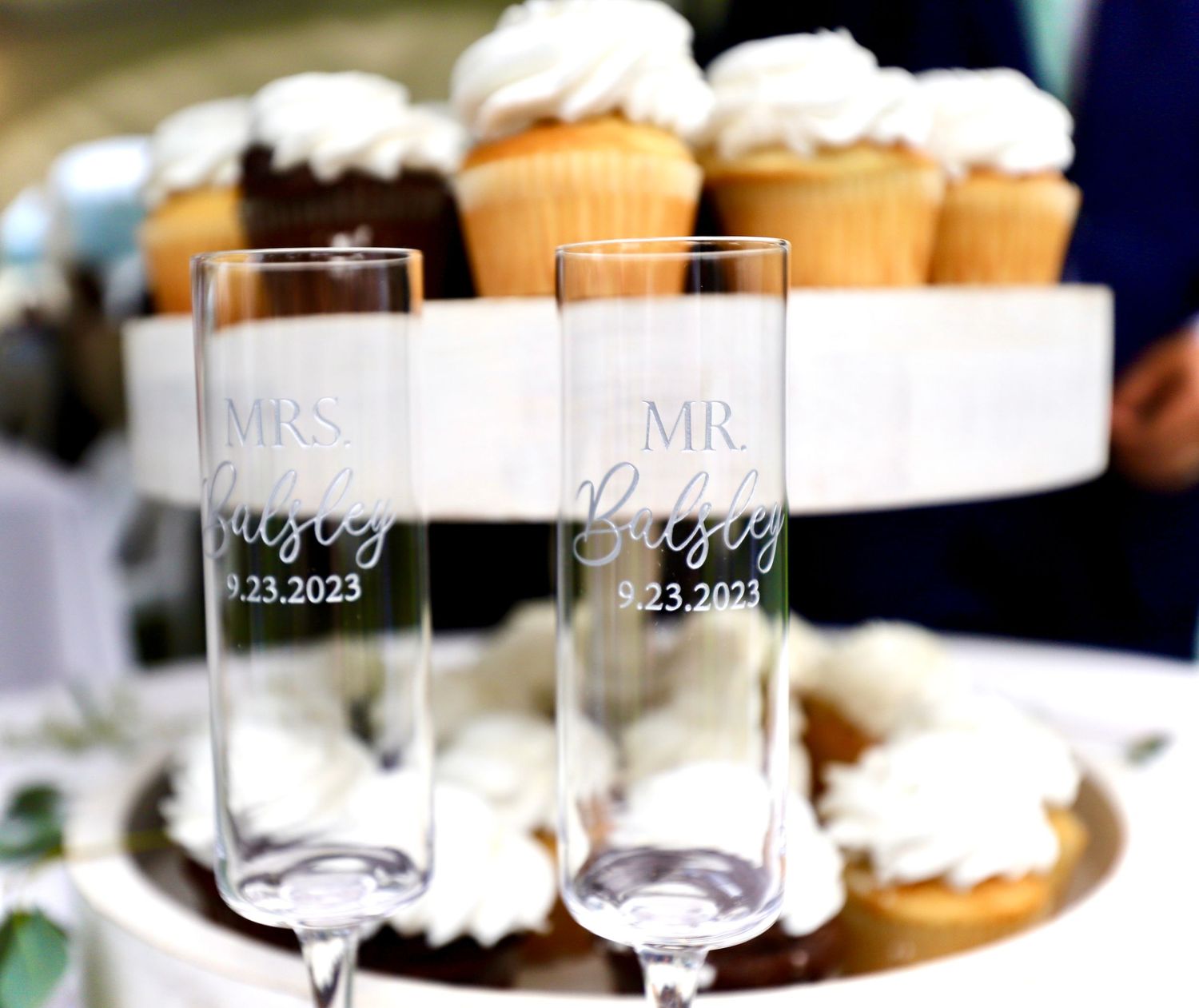 Personalized Mr. and Mrs. Buisey champagne flutes dated 9.23.2023 displayed in front of wedding cupcakes.