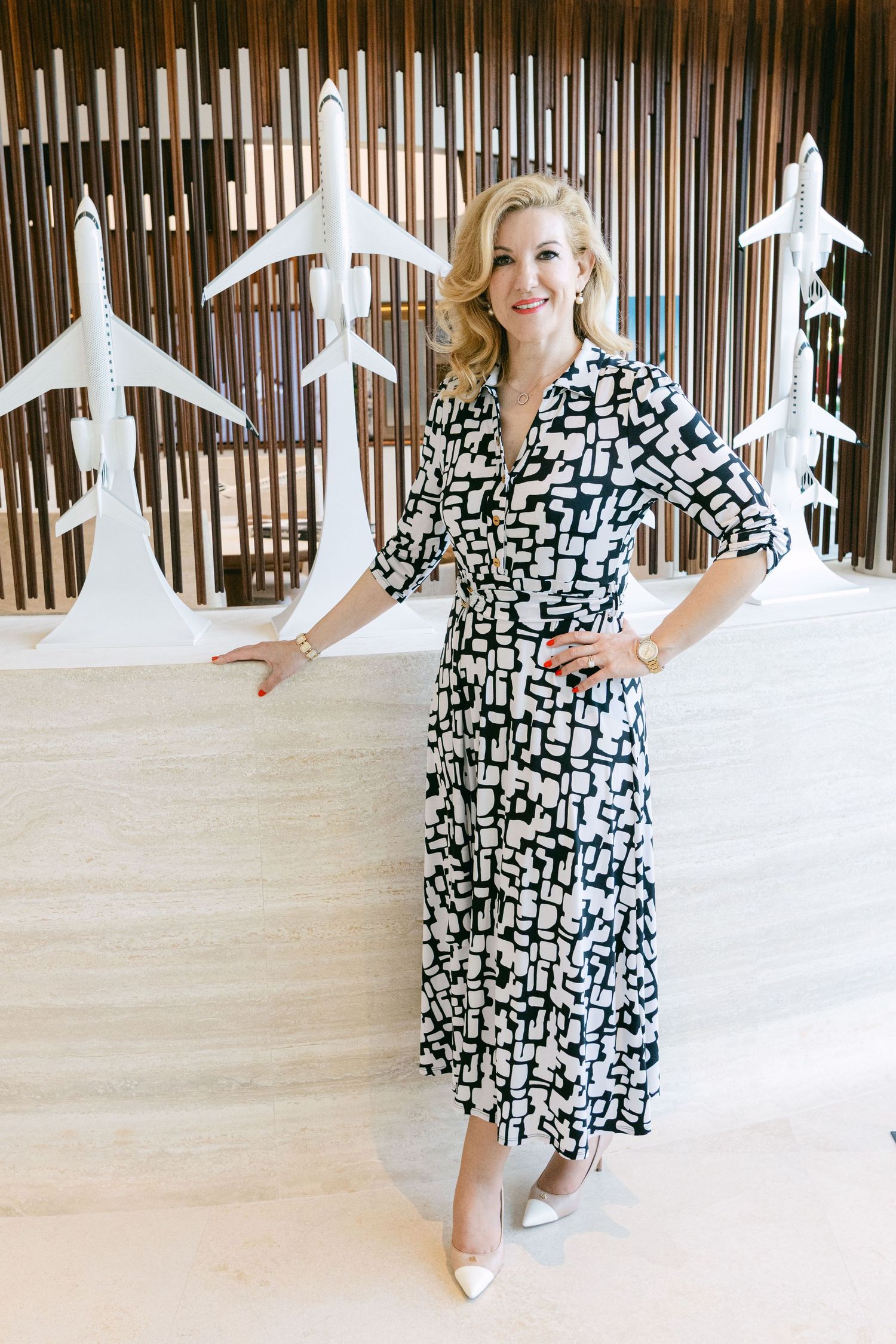 A woman in a black and white geometric print dress poses in a sequence of dance moves against a wooden slatted wall.