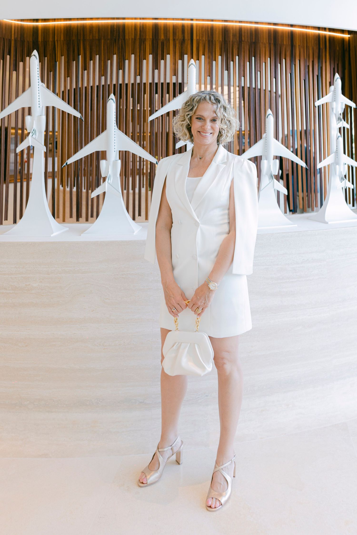 A series of four photos showing someone in a white outfit posing against a wooden wall with airplane silhouettes.