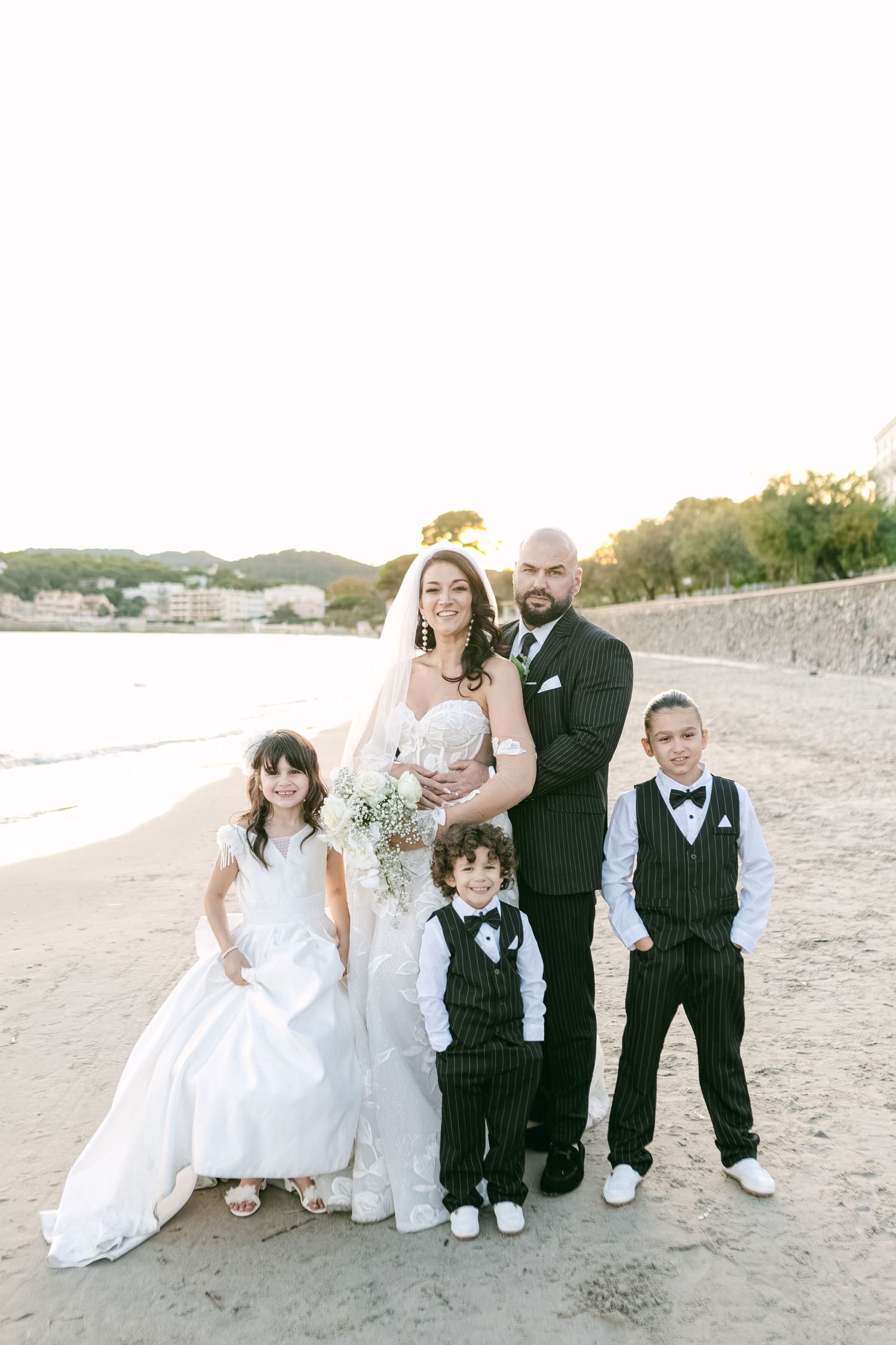 Wedding party poses on sandy beach at sunset wearing black and white formal attire.