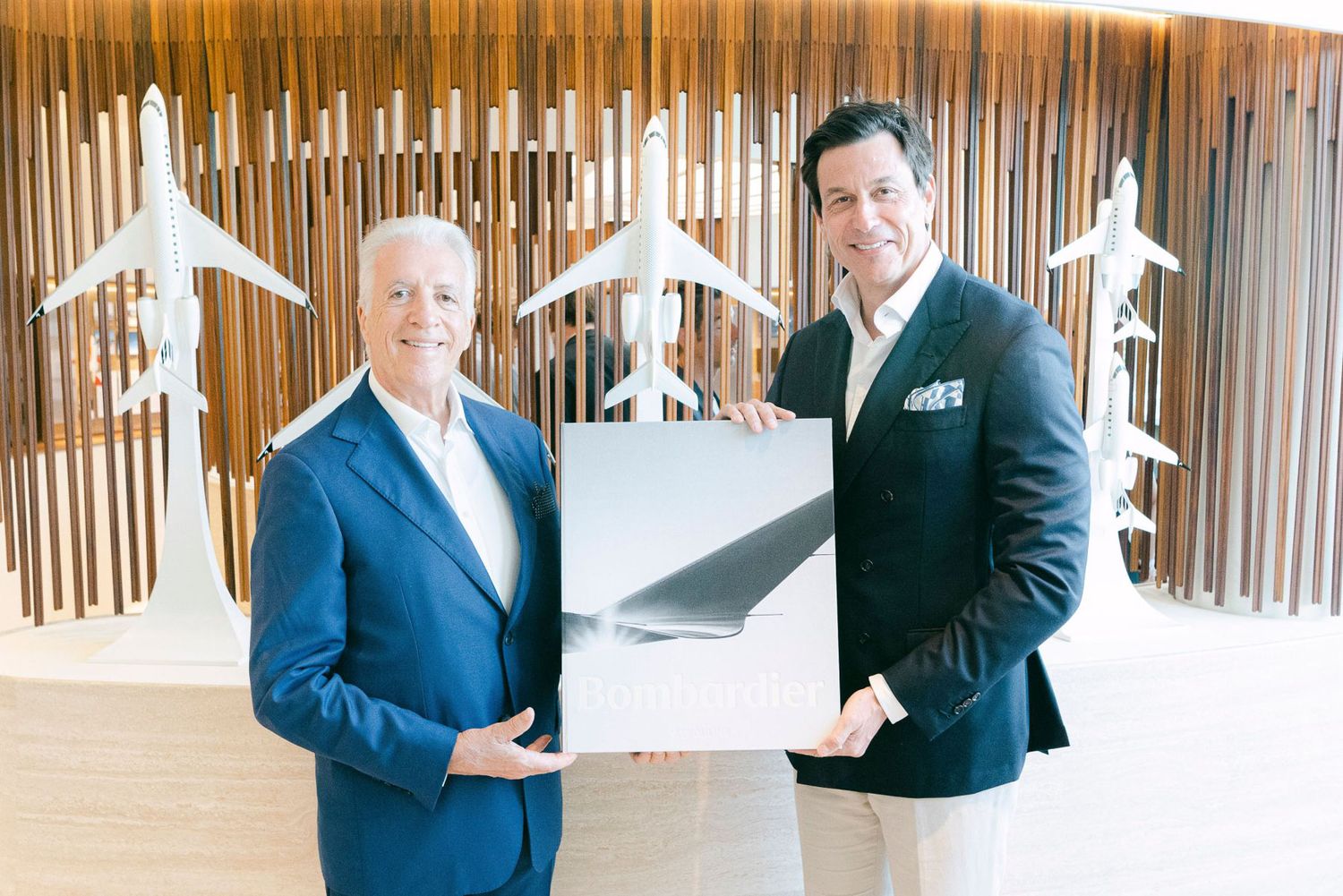 Business professionals in dark suits stand in front of a wooden wall display with decorative white airplane models.