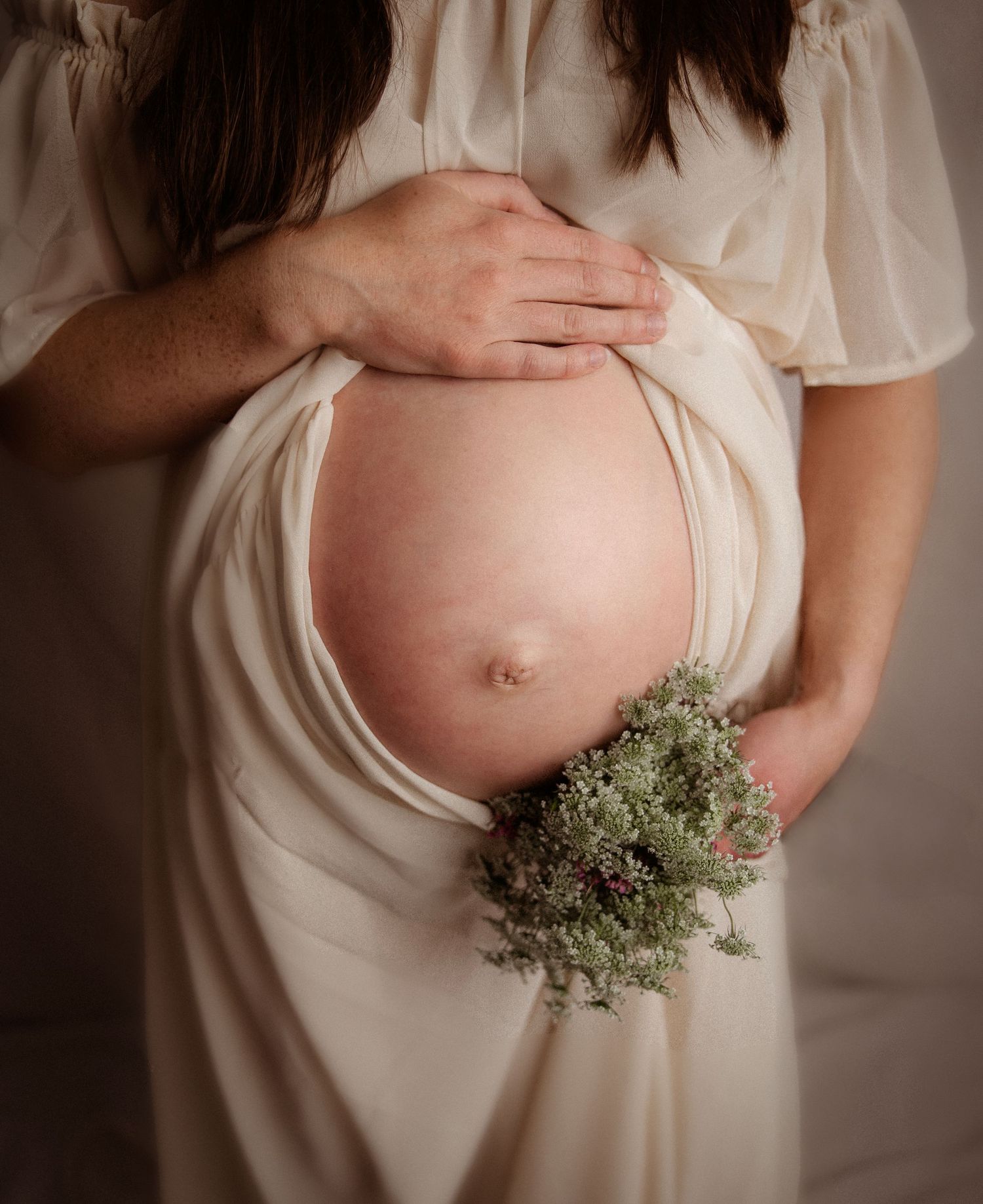 Pregnant woman holding flowers and belly in Portland Oregon studio