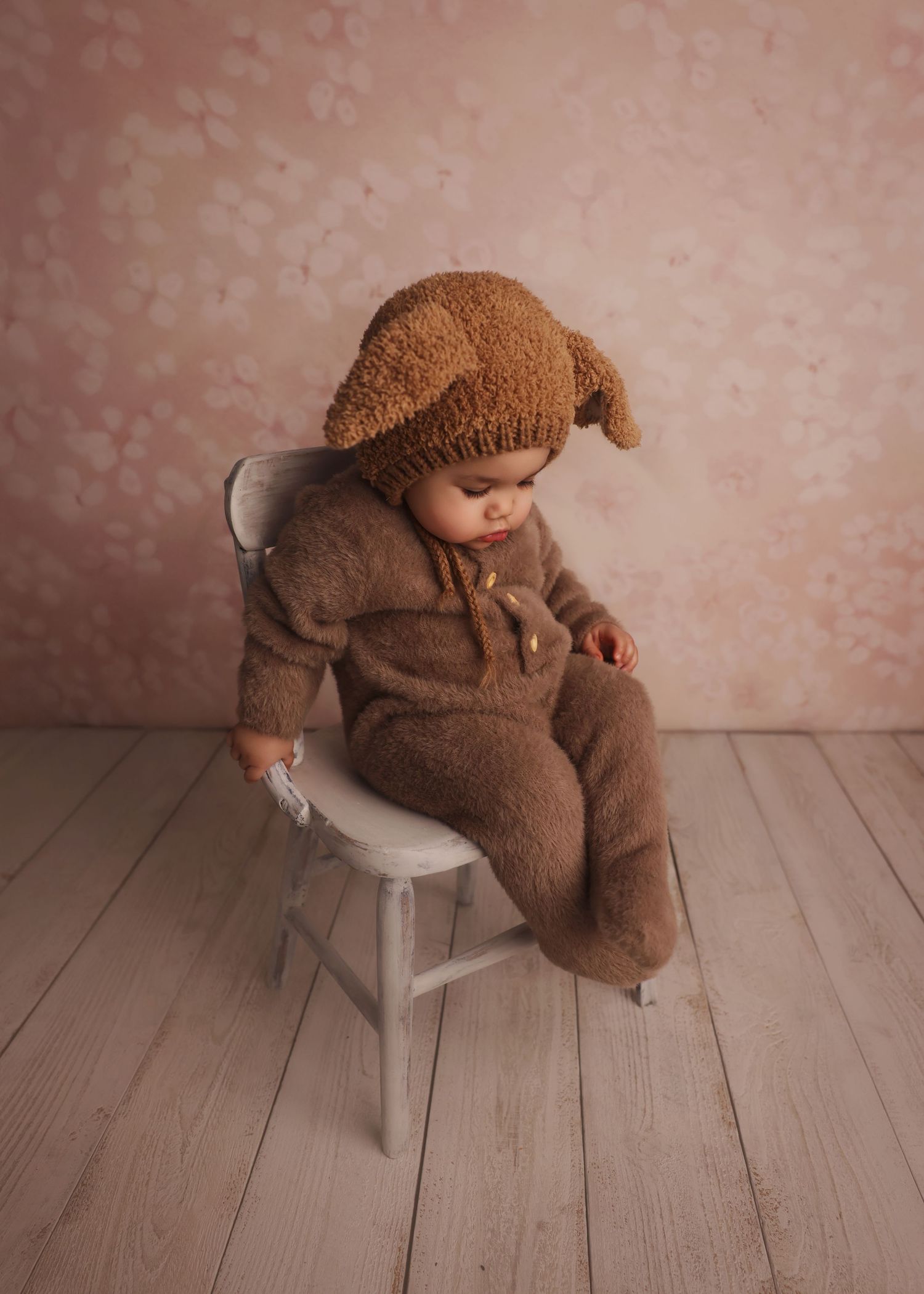 Baby wearing teddy bear outfit sitting on chair for milestone photoshoot