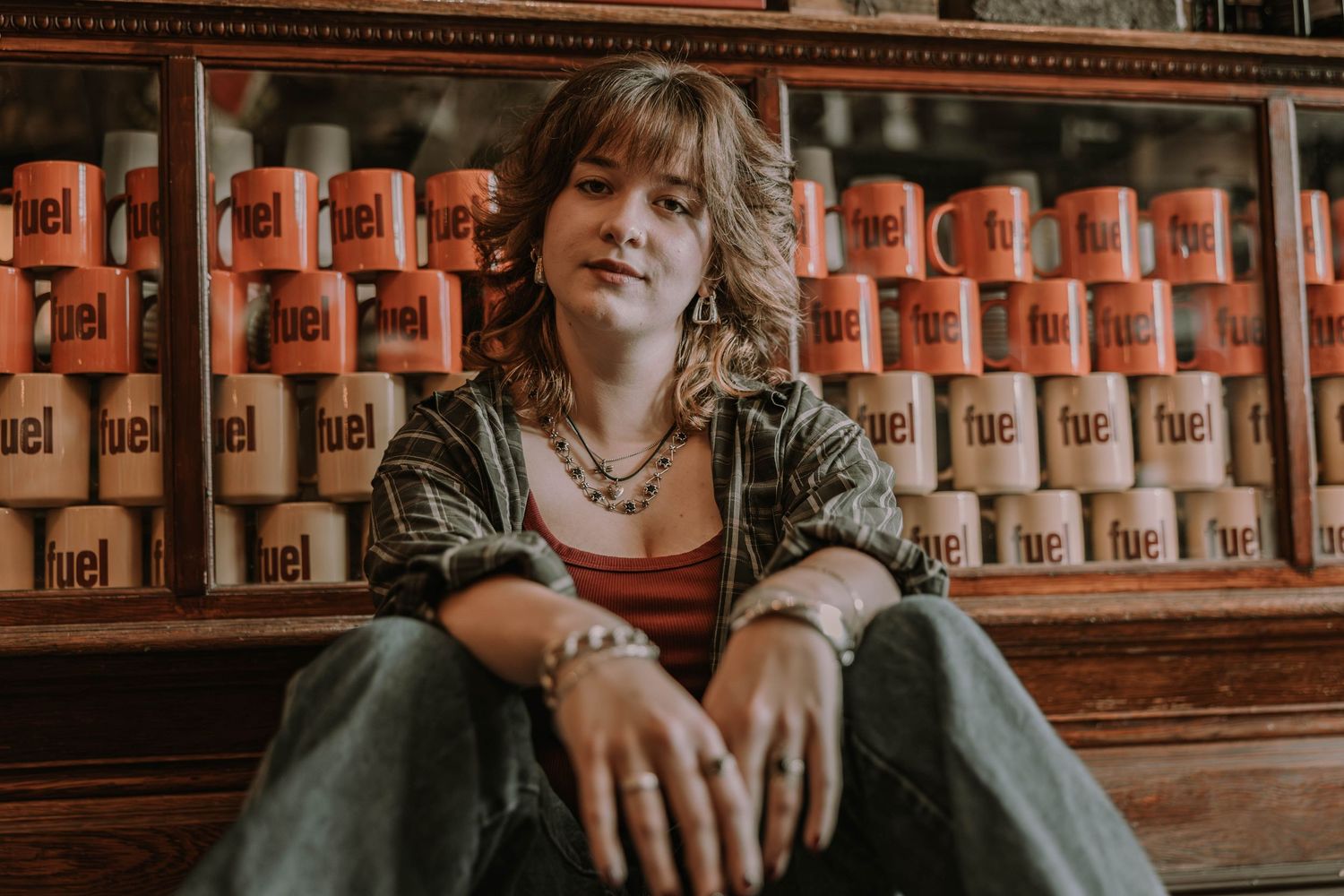 Someone sits casually against a wall lined with vintage orange metal fuel or oil cans in warm lighting.
