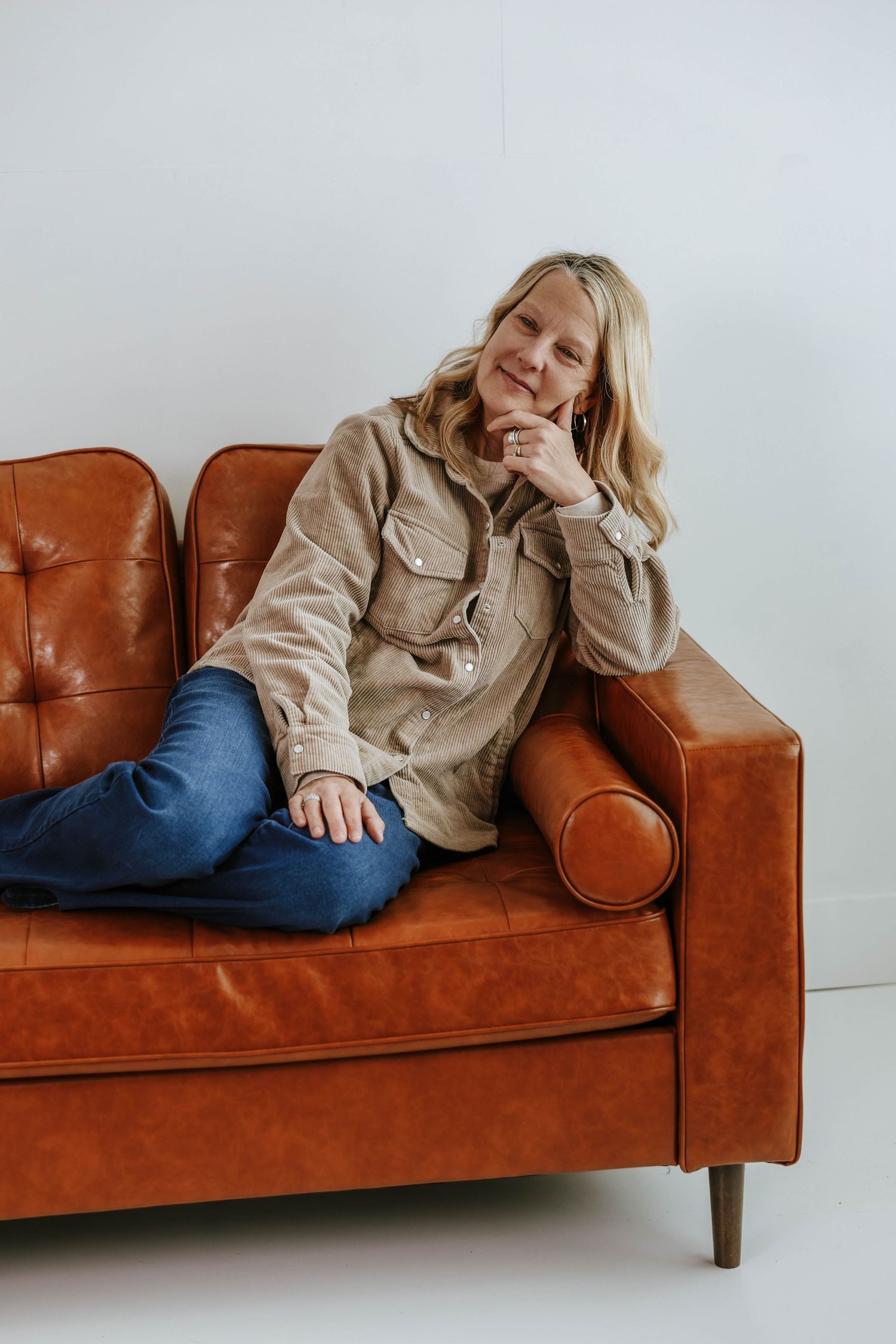 Relaxed lifestyle portrait on vintage leather sofa against minimalist white background.