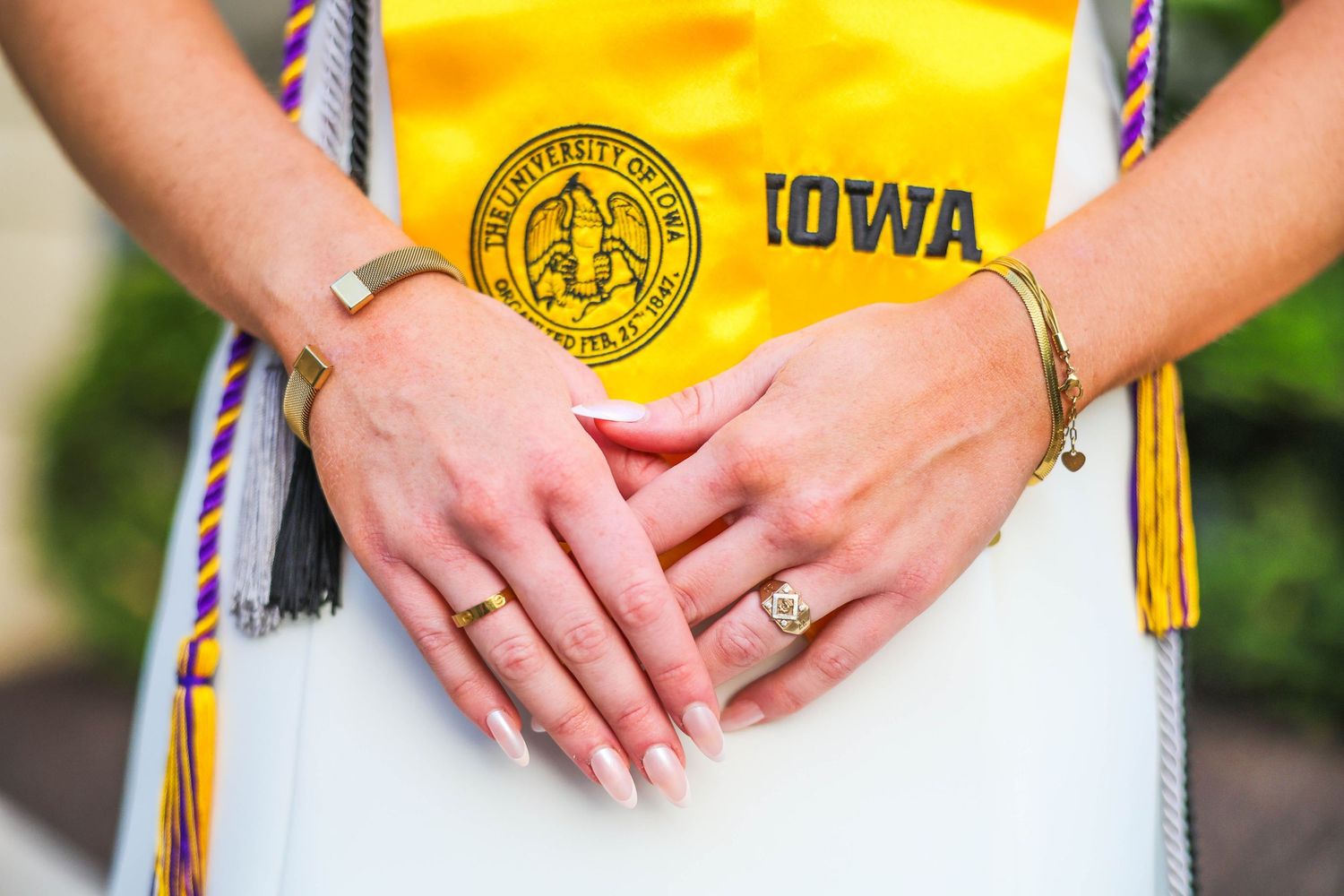 A close-up of hands wearing a graduation ring and yellow Iowa university stole with emblem.