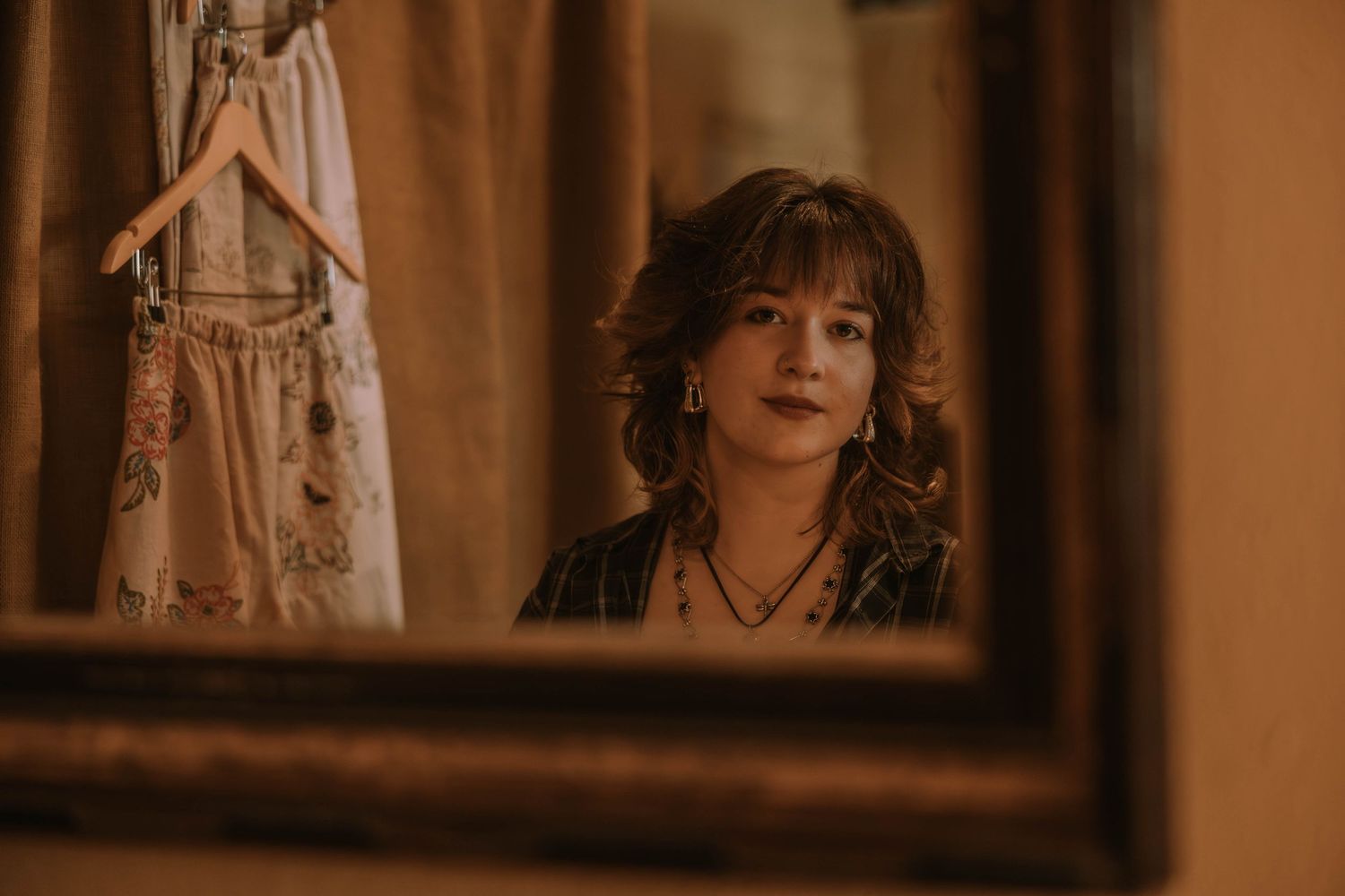 A warm-toned vintage style mirror reflection showing a figure with curly hair in an intimate indoor setting.