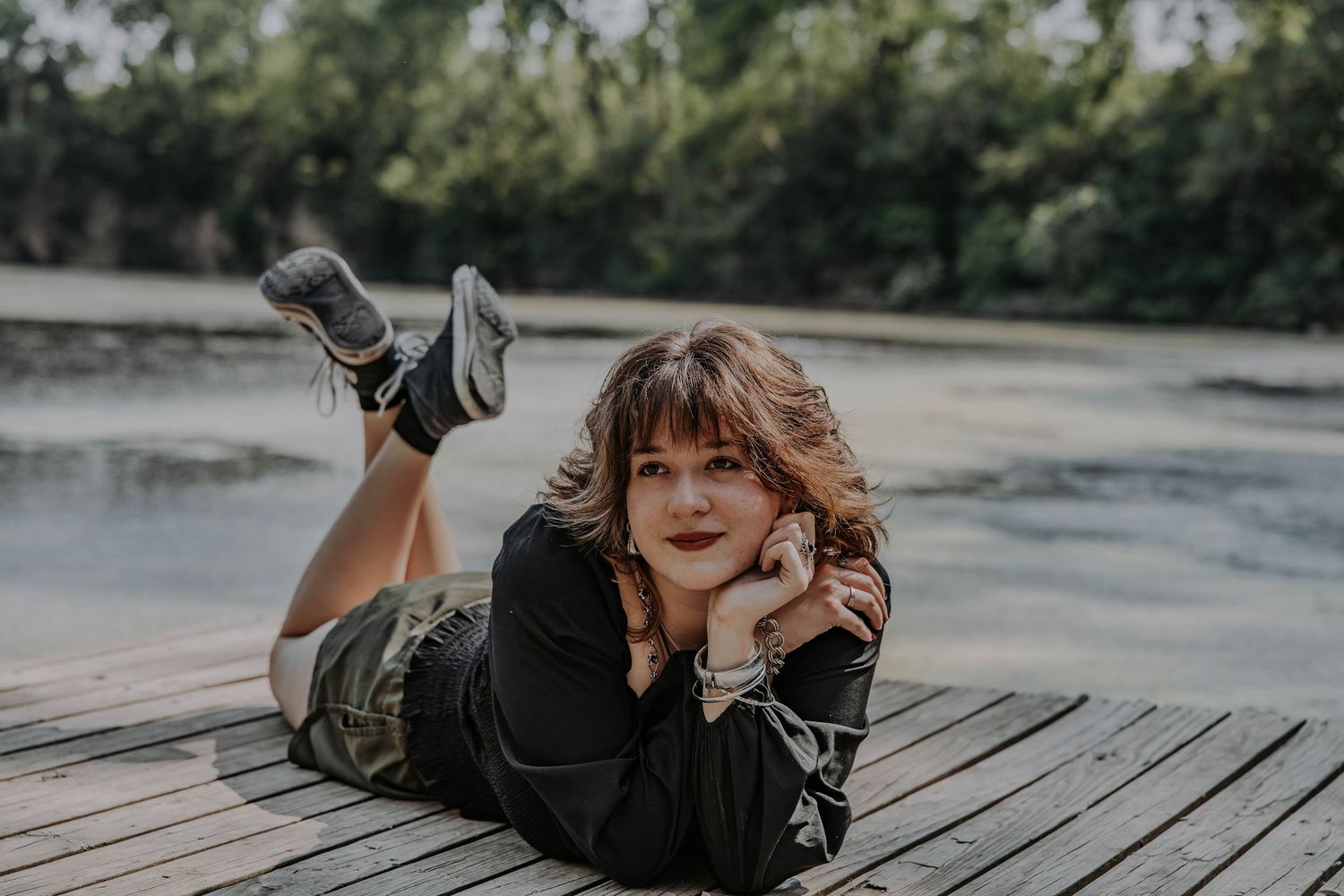 A person lying on a wooden dock wearing combat boots and casual clothing on a sunny day.