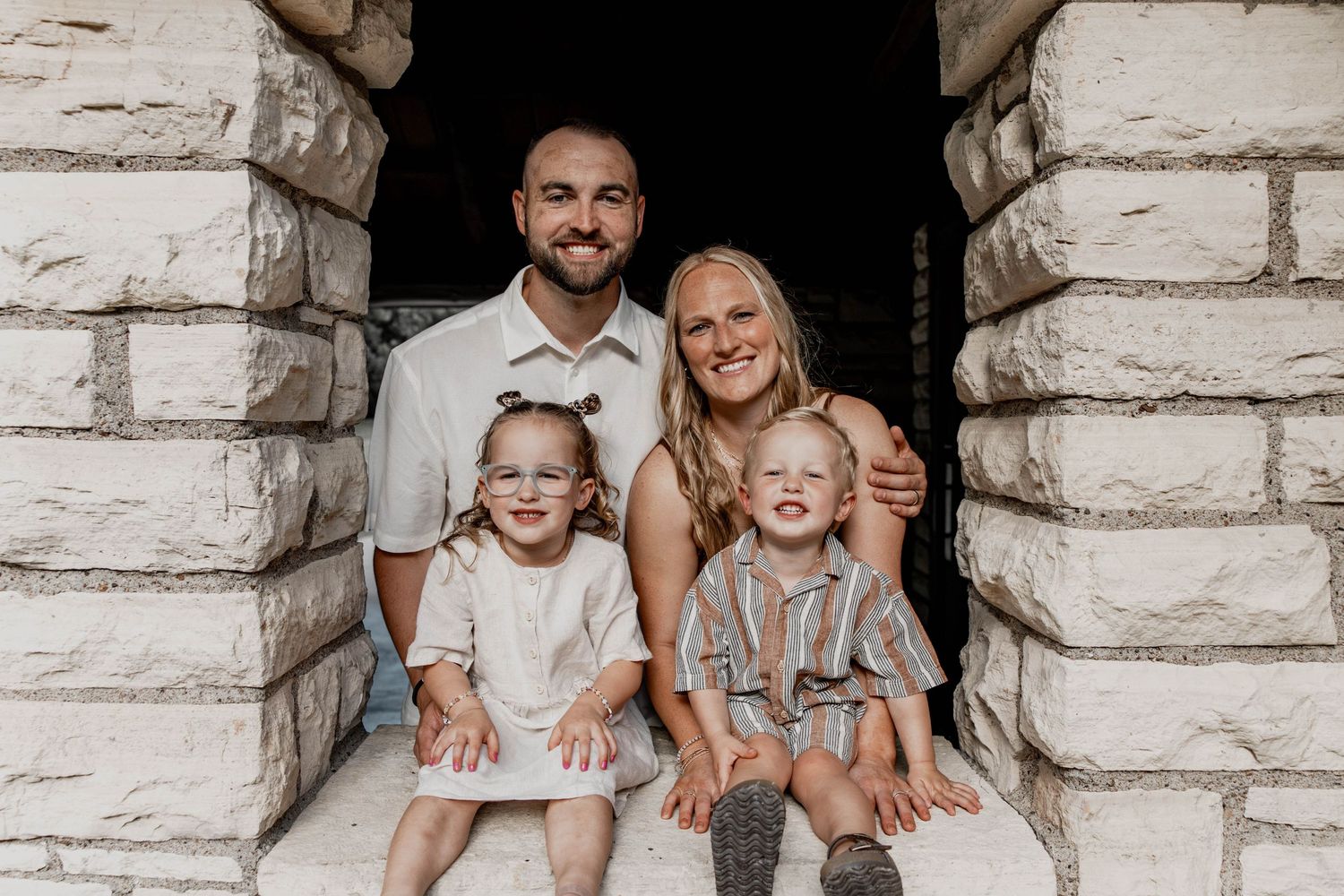 Family wearing white outfits poses together against white brick wall in a series of candid shots.