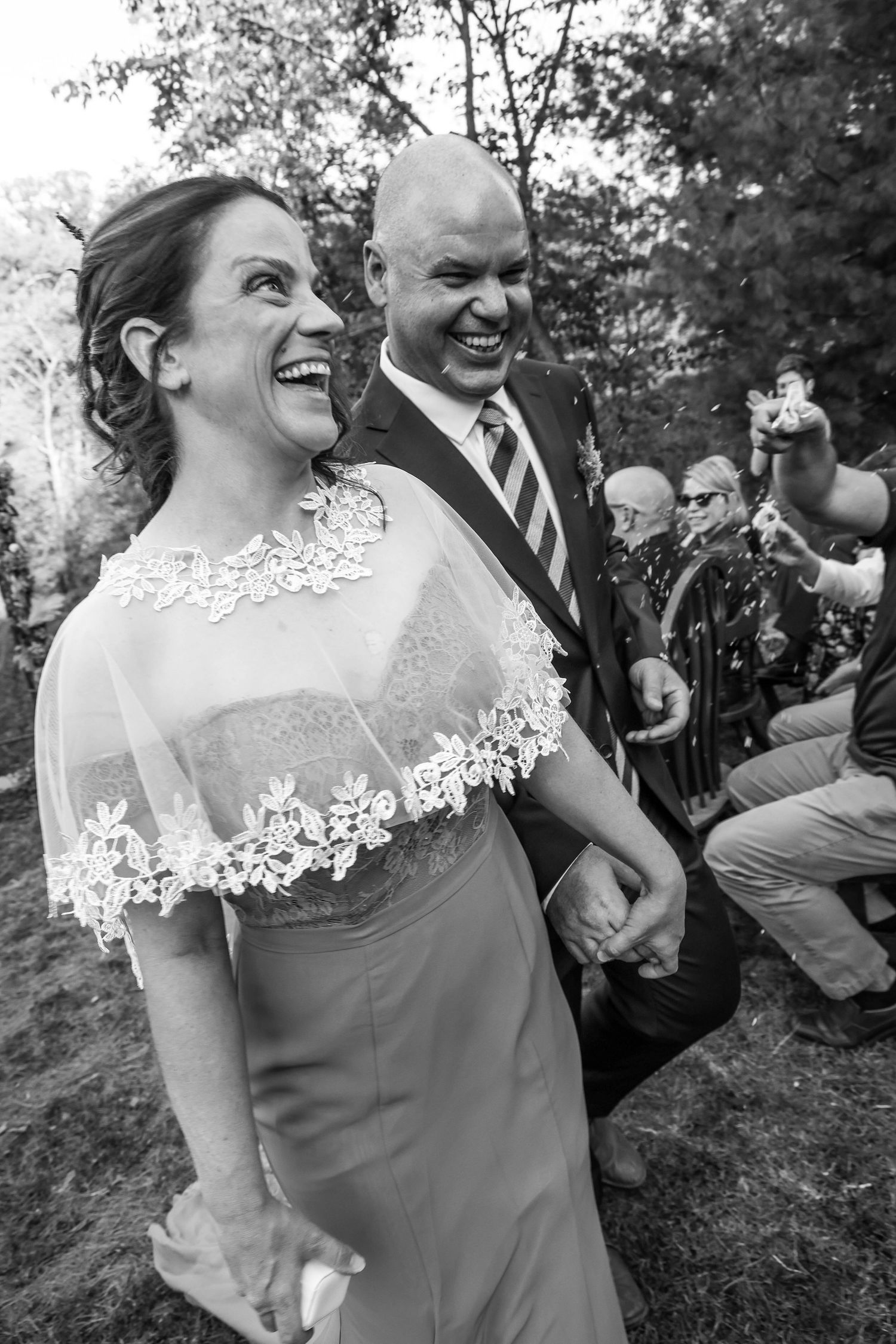 Black and white photo capturing a joyful moment at a wedding as couple laughs together during outdoor ceremony.