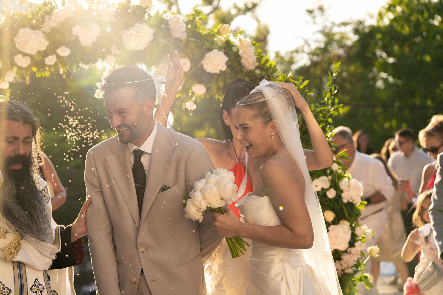 Wedding celebration at sunset with guests in beige and white attire enjoying champagne outdoors.