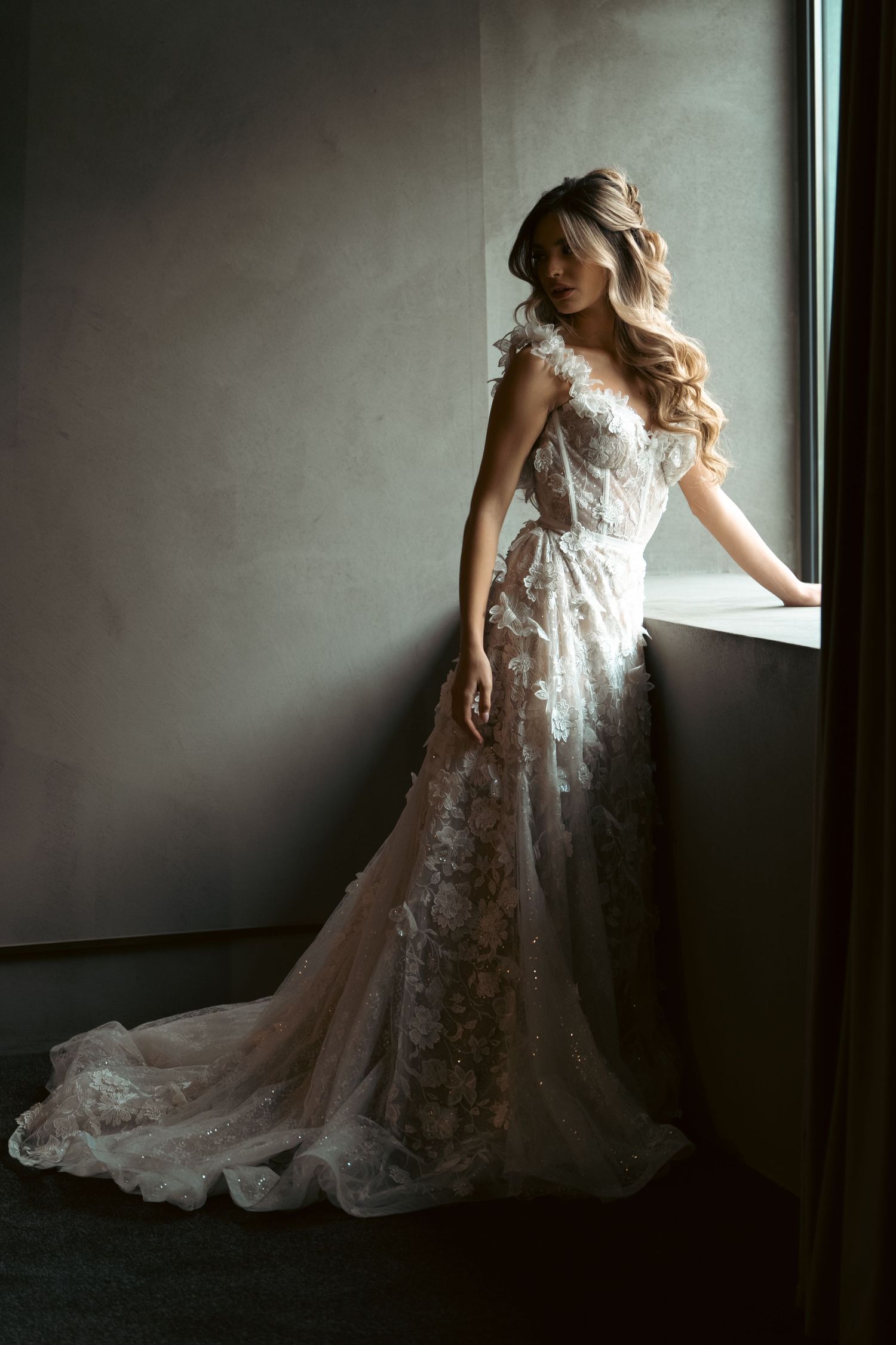 Wedding dress with intricate lace details captured in moody window light.
