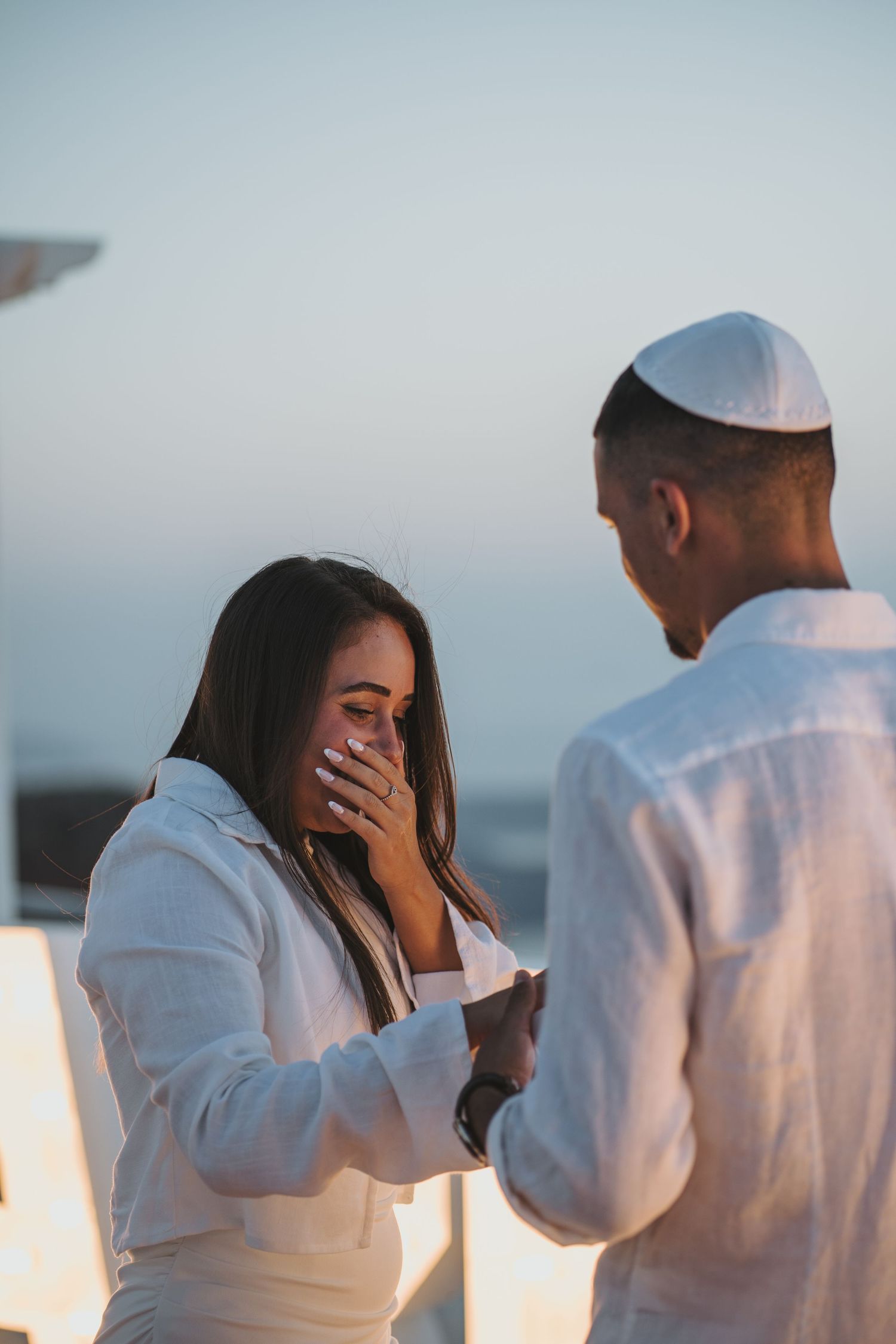 Emotional marriage proposal scene at sunset with surprised reaction in Santorini Greece