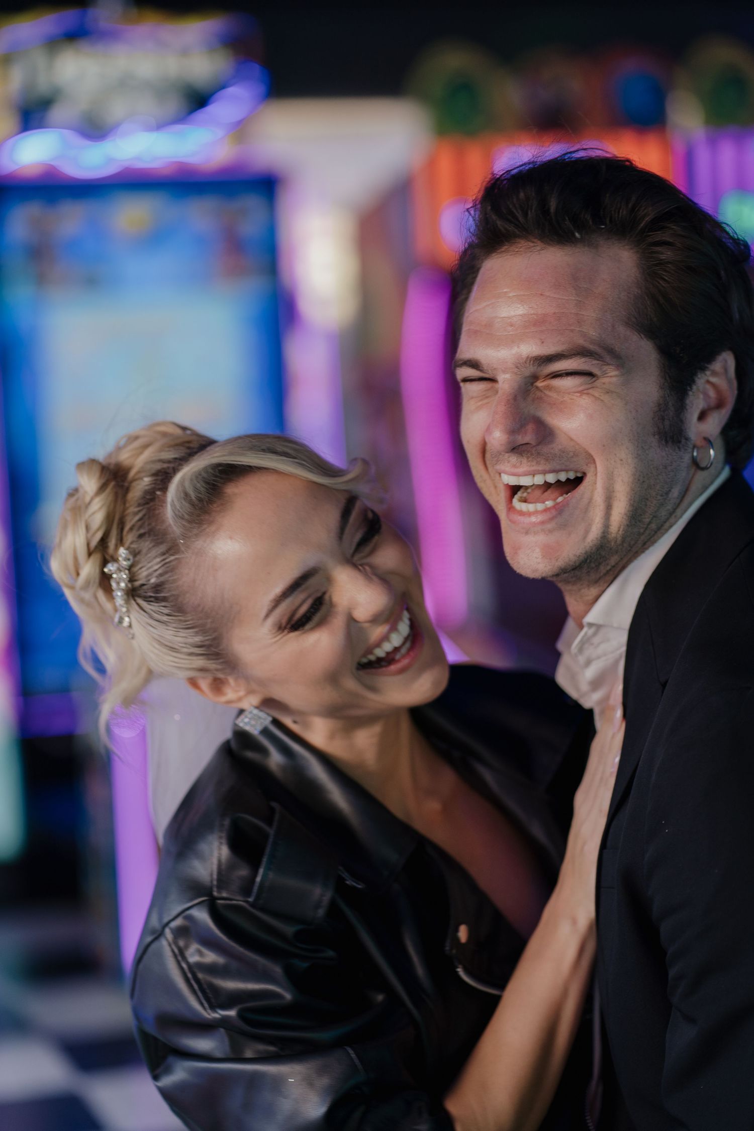 A married couple sharing a genuine laugh together in front of colorful arcade lights.
