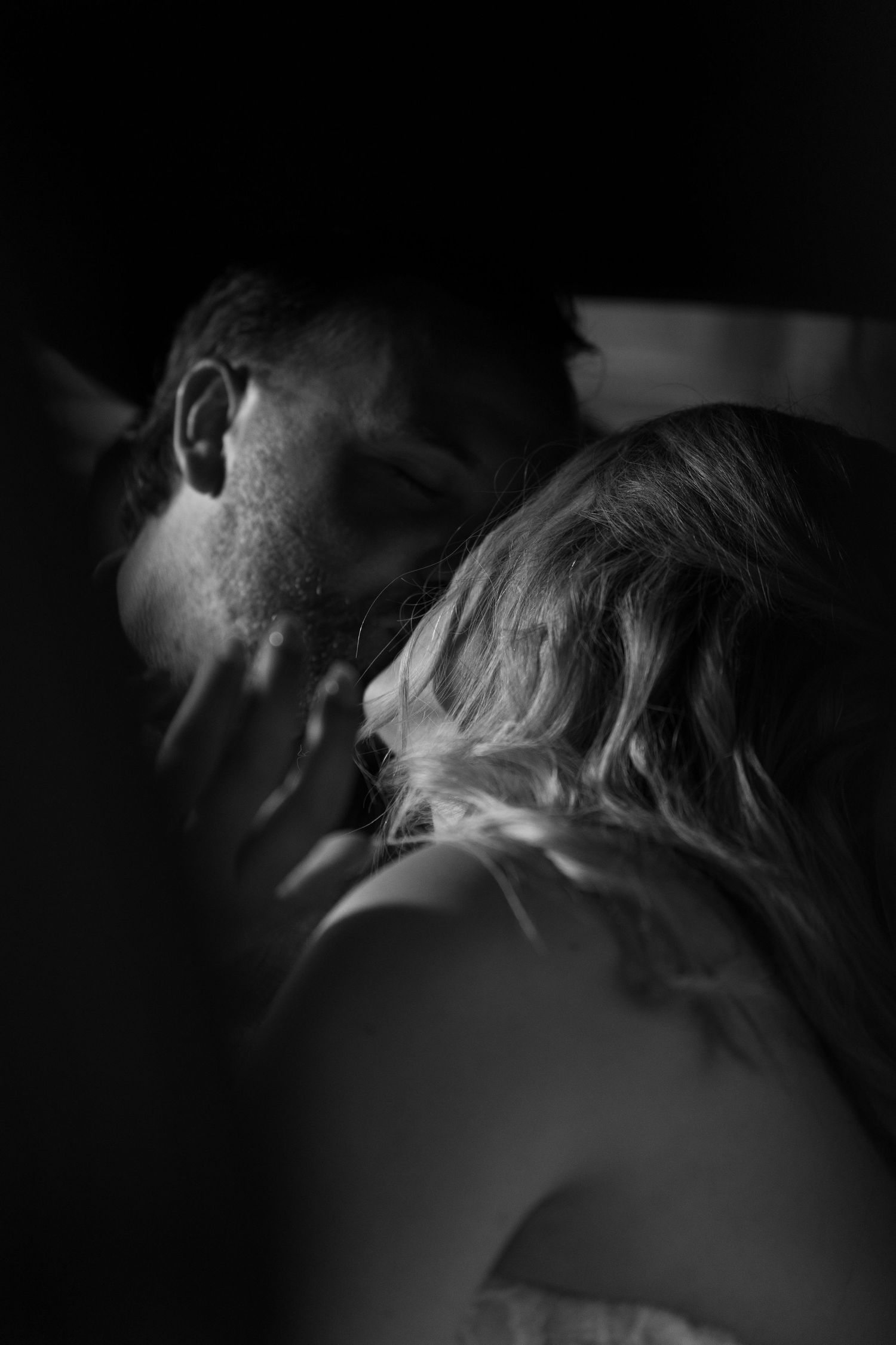 Intimate black and white photograph of a tender moment between two people in shadow.