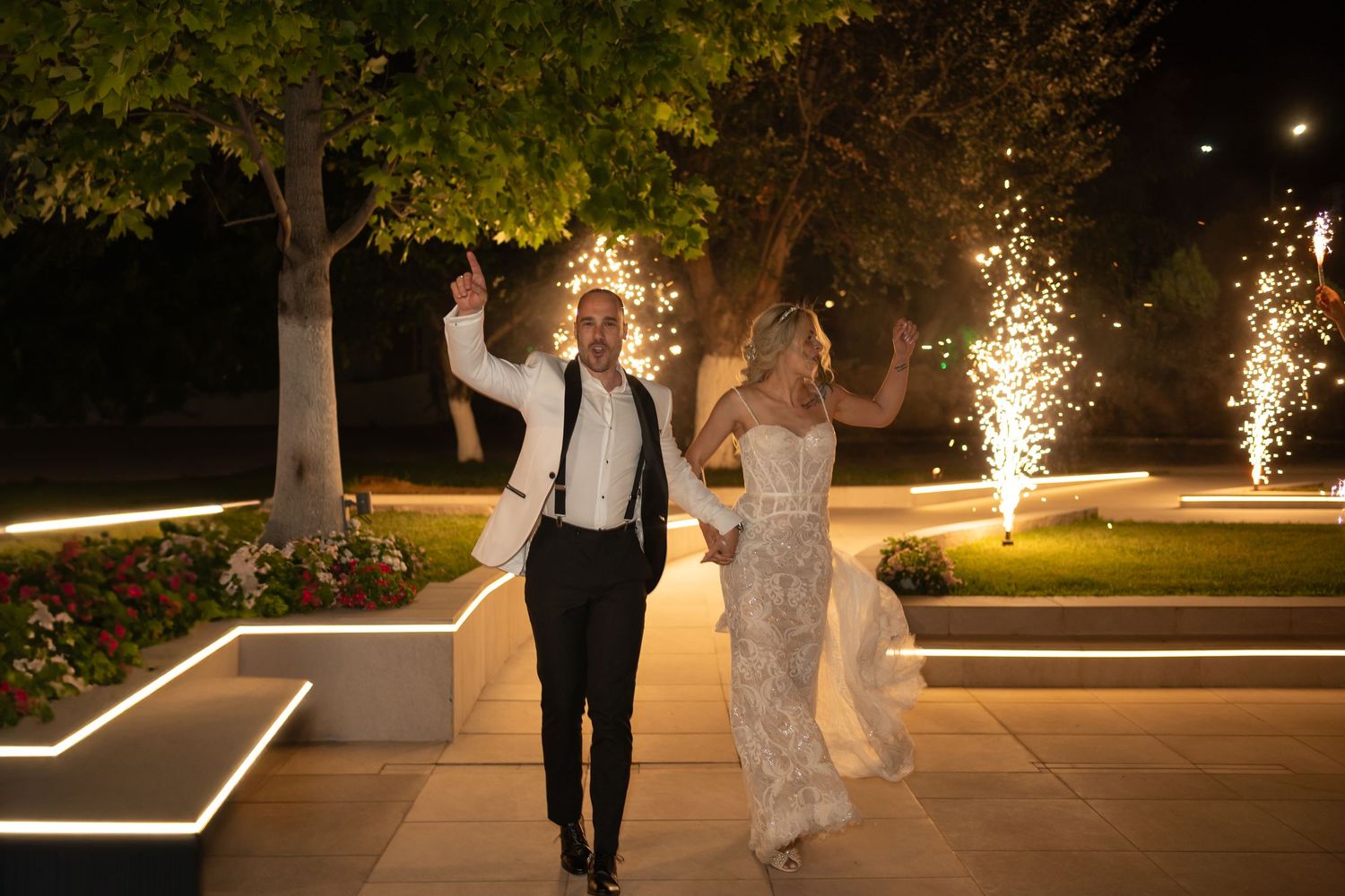 Wedding couple walking along an illuminated outdoor pathway with sparklers at night.